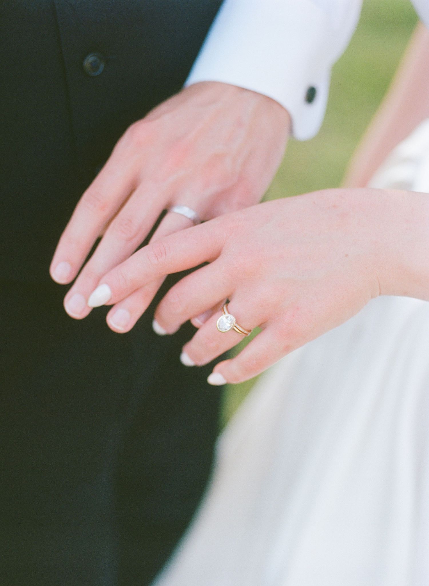 Close-up of newlyweds hands showing a gold engagement ring and wedding bands on their ring fingers.