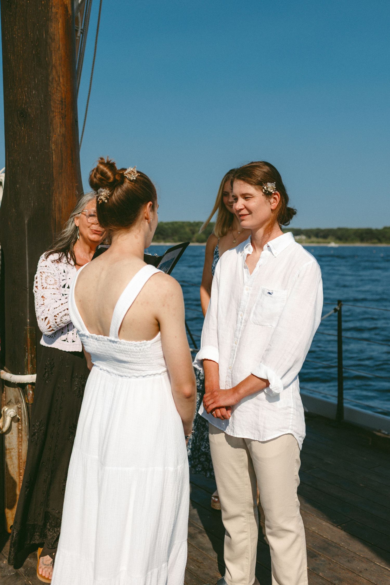 Wedding ceremony participants gather on the deck of a sailing vessel with water and coastline visible.