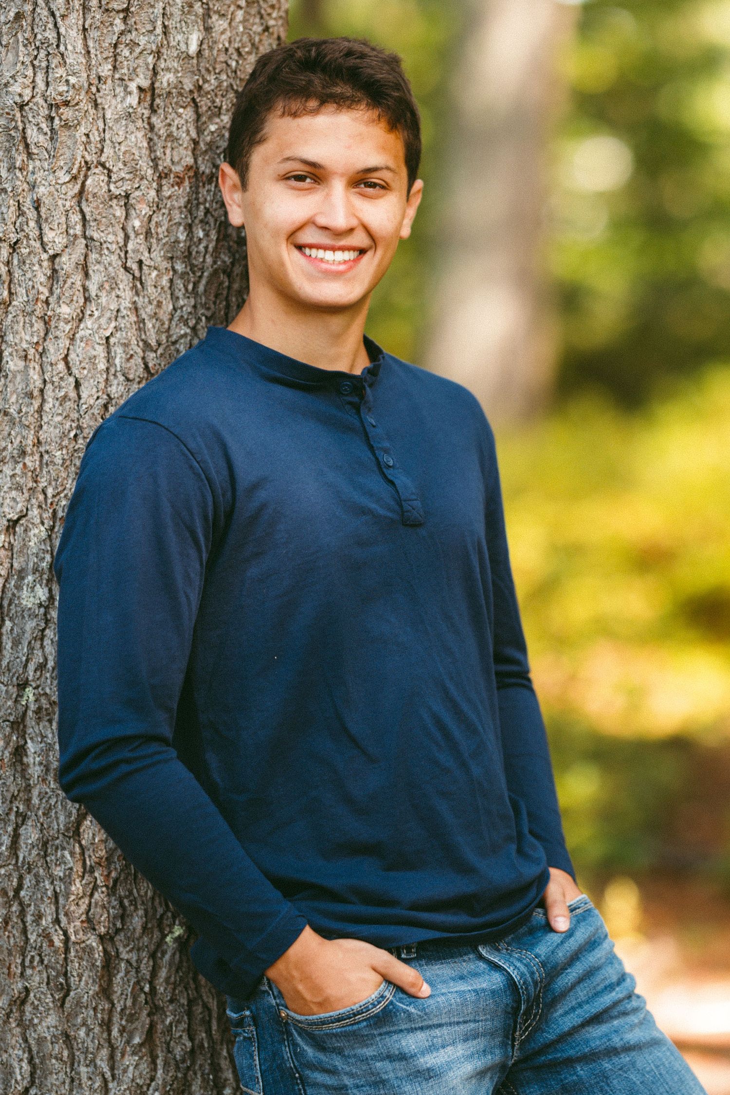 Casual portrait against a tree trunk in natural outdoor setting.