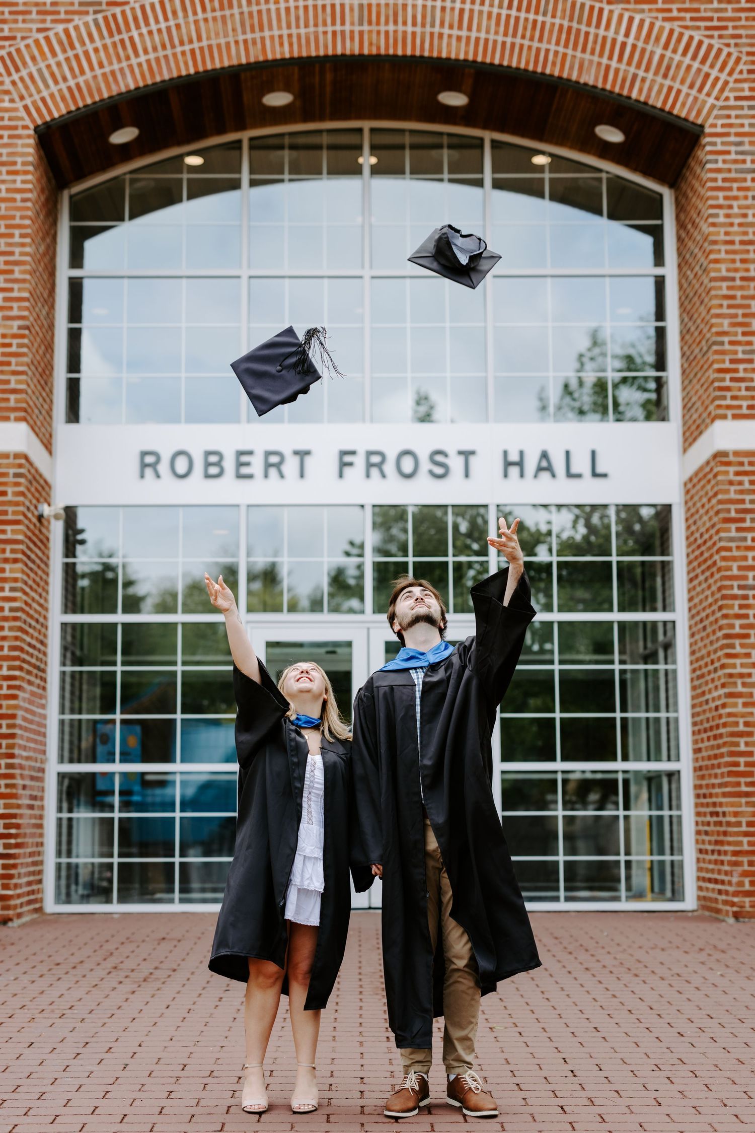 Graduates celebrating in front of Robert Frost Hall with caps thrown in the air.