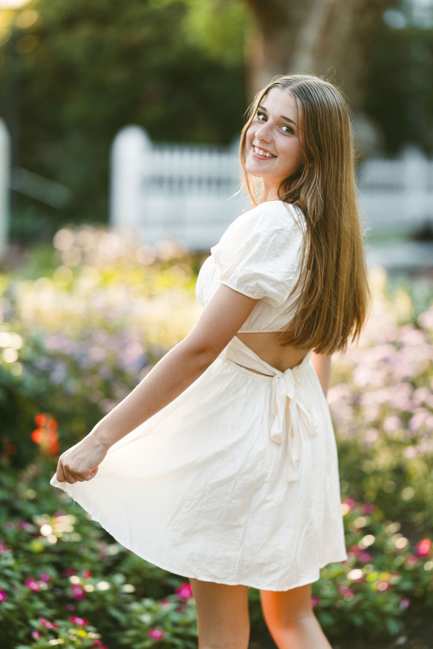 Young person in white dress dancing in a garden with blooming flowers.