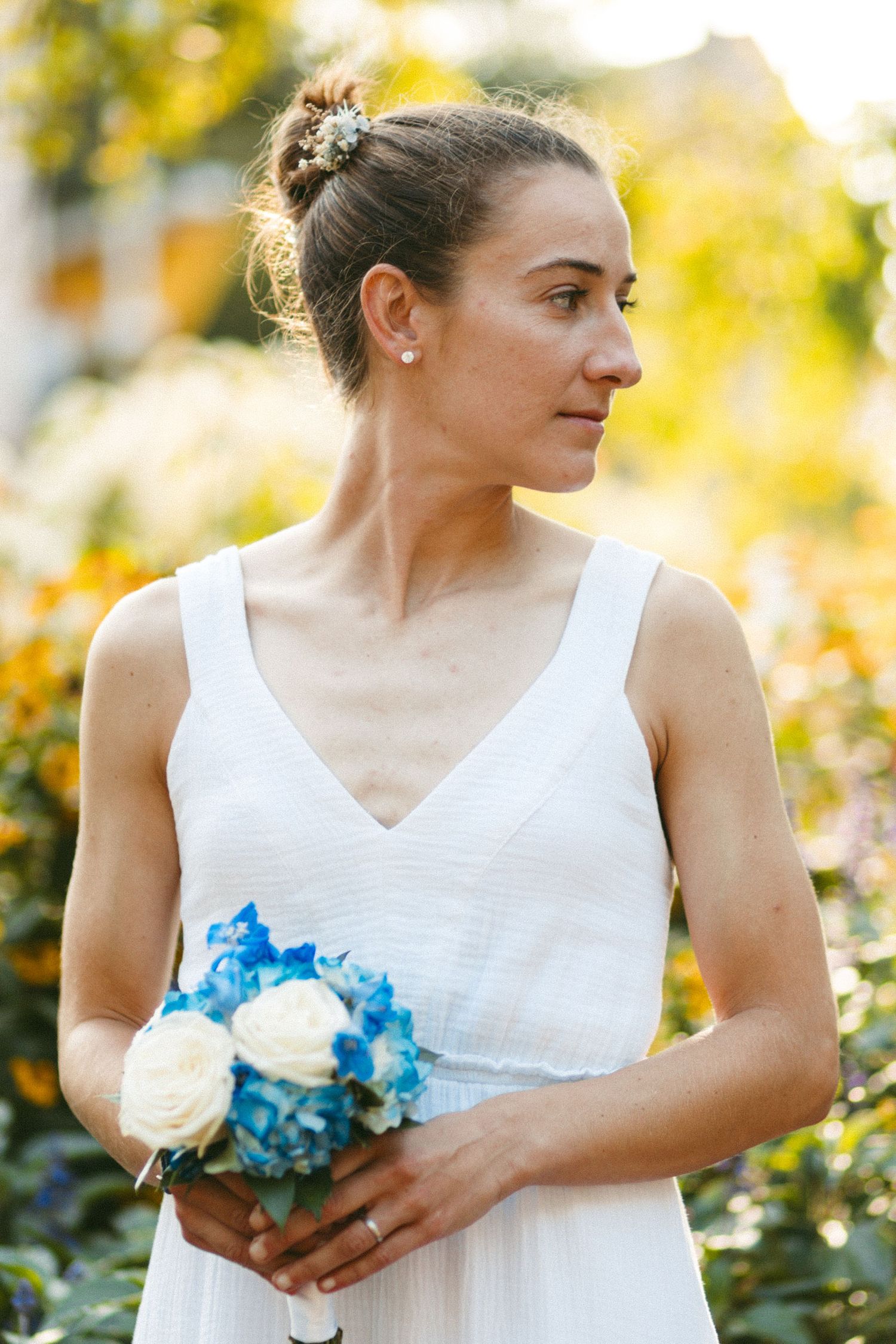 Bride in white dress holding blue hydrangea bouquet in garden setting.
