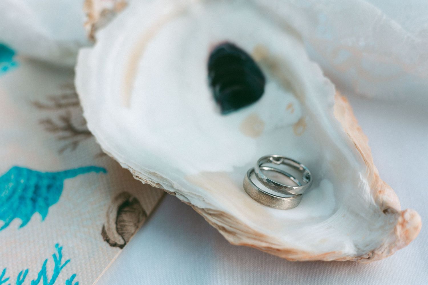 Close-up detail of wedding rings nestled in oyster shells with turquoise decorative elements.