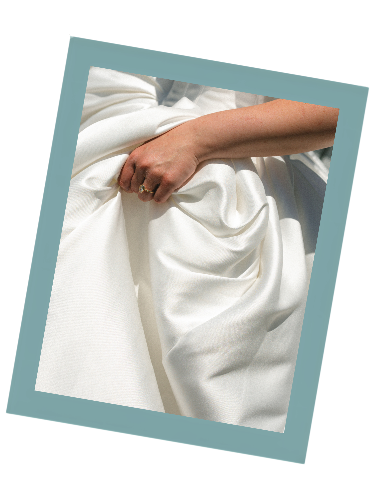 A hand with a ring gently gathers flowing white satin fabric, perfect for bridal or luxury textile inspiration.