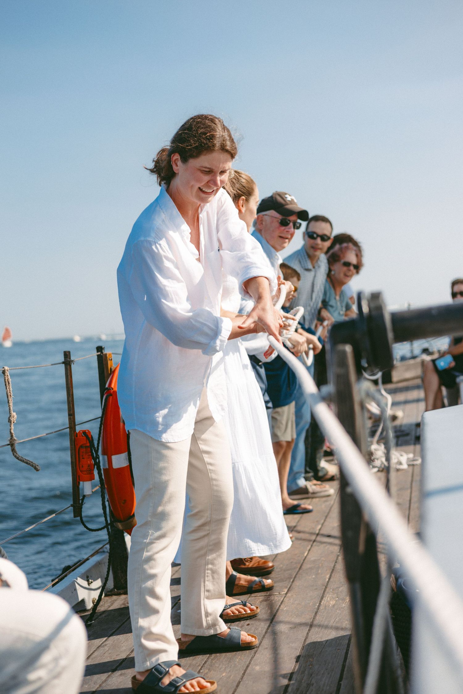 People in white and casual attire gather on a sunny dock by the water.