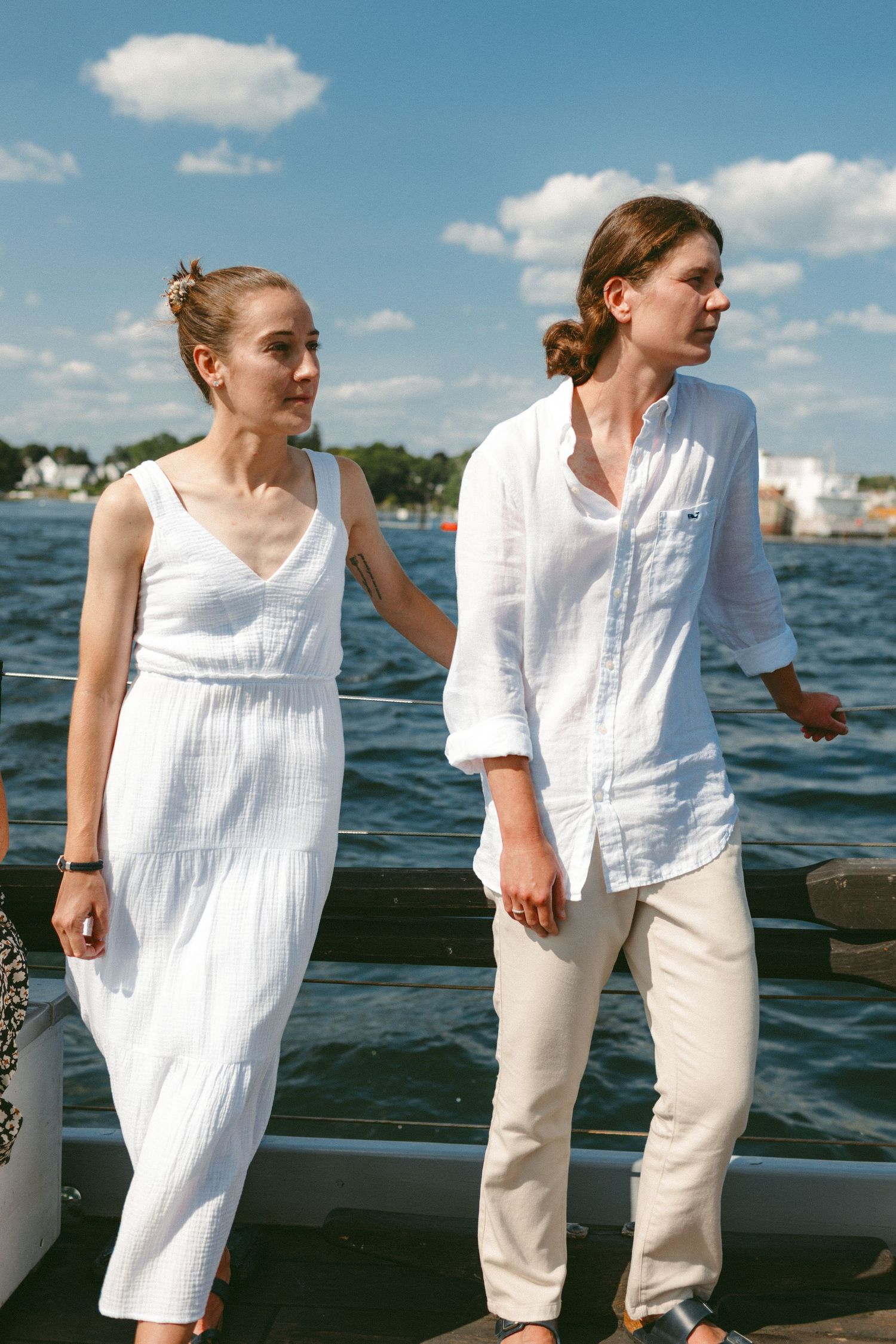 People in white summer clothing standing on a boat deck against a blue sky.
