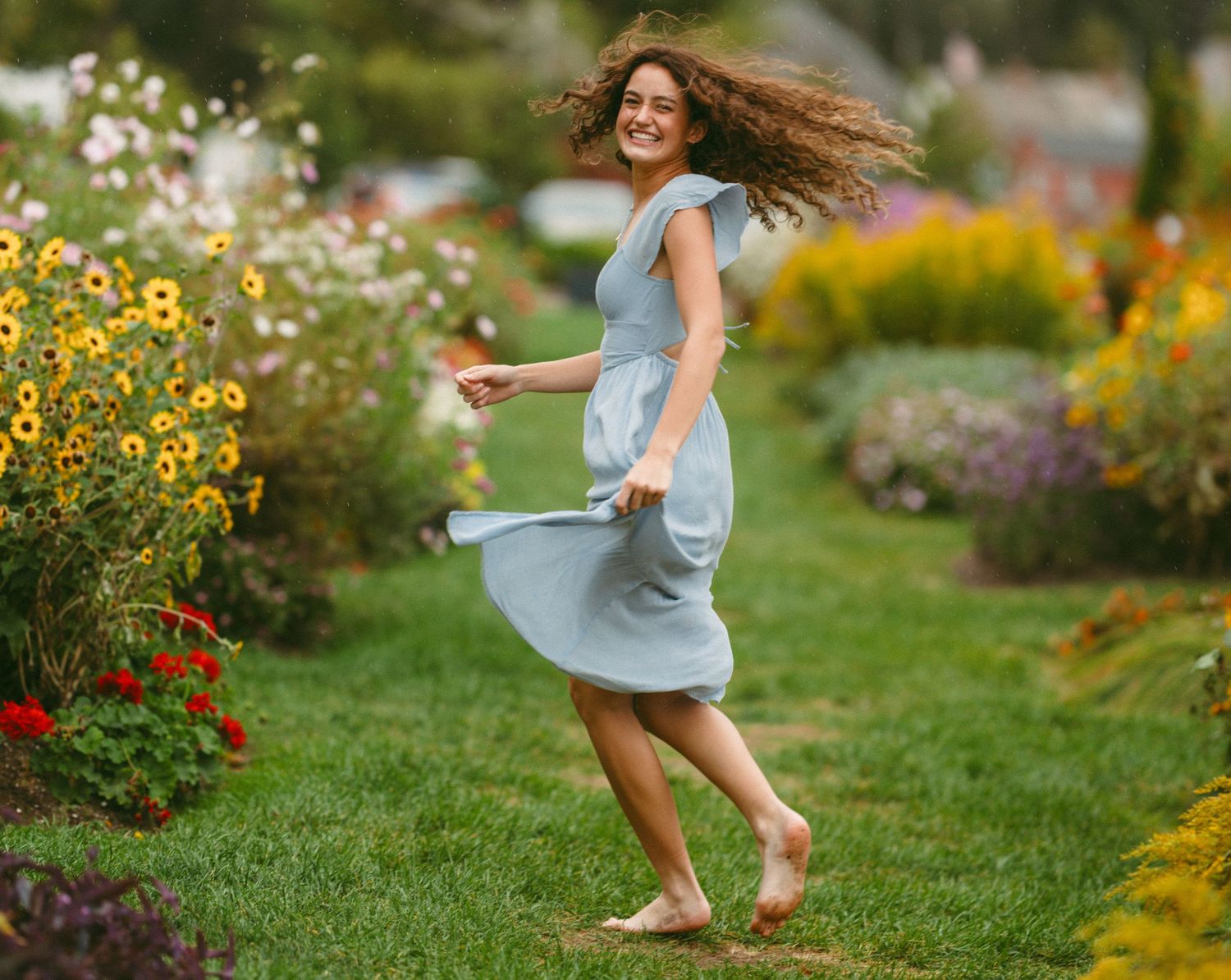 Playful movement captured in a flowing blue dress against a colorful garden backdrop.
