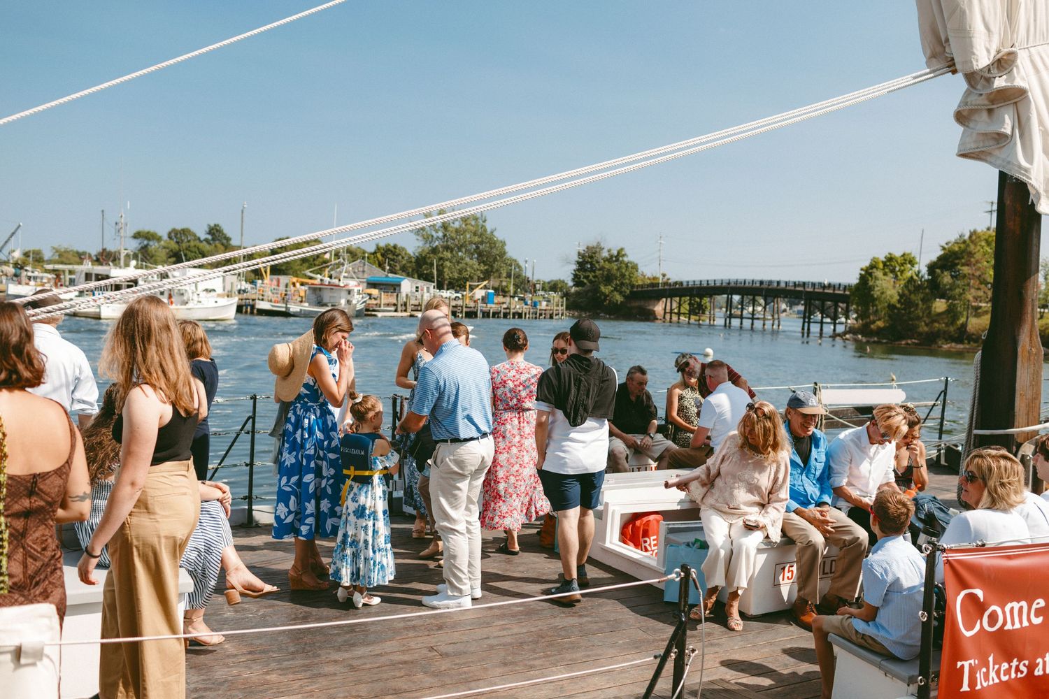 Wedding guests gather on a waterfront dock during a sunny outdoor celebration.