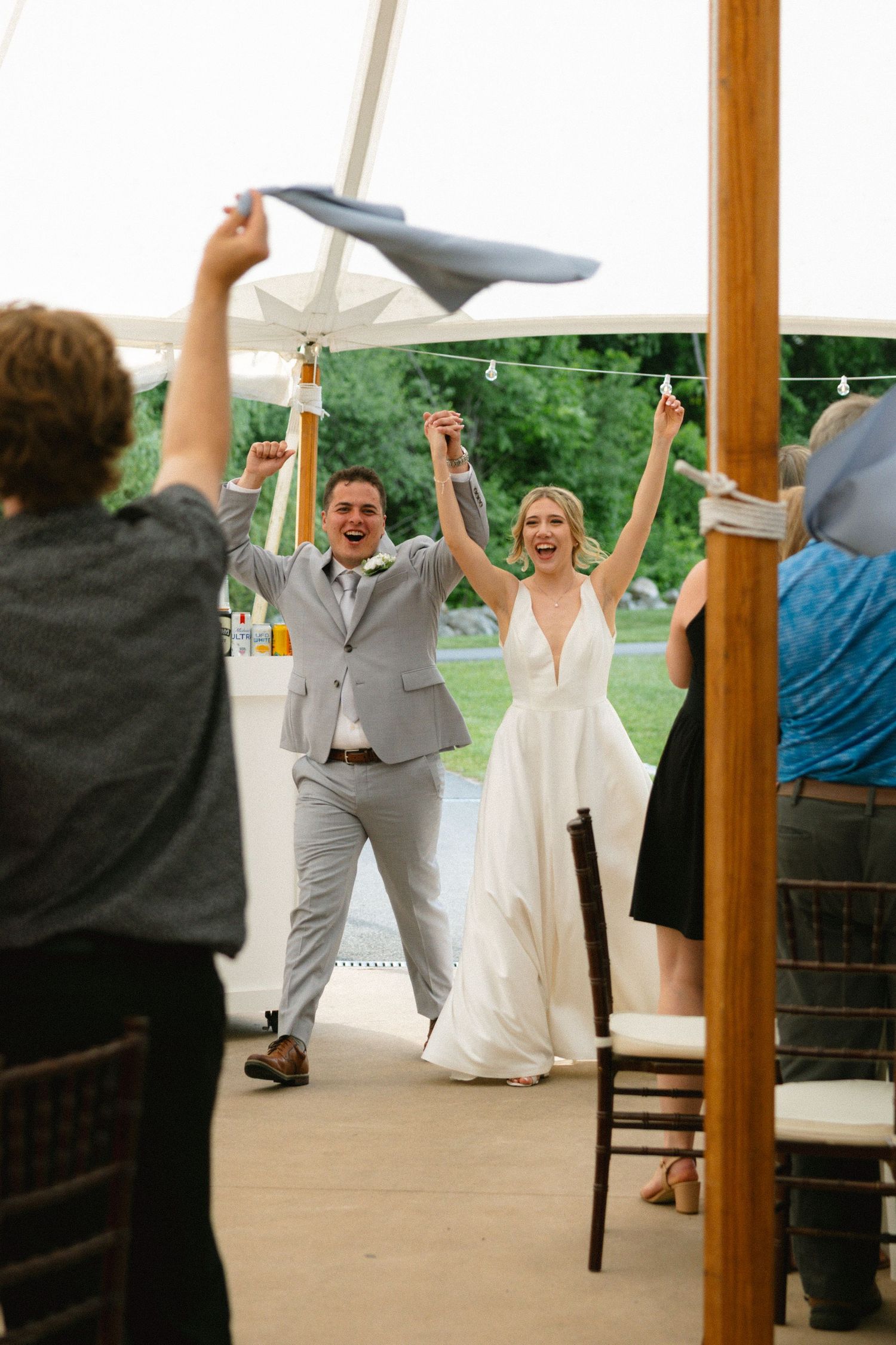 Excited newlyweds raise hands in celebration as they enter their elegant tented wedding reception.
