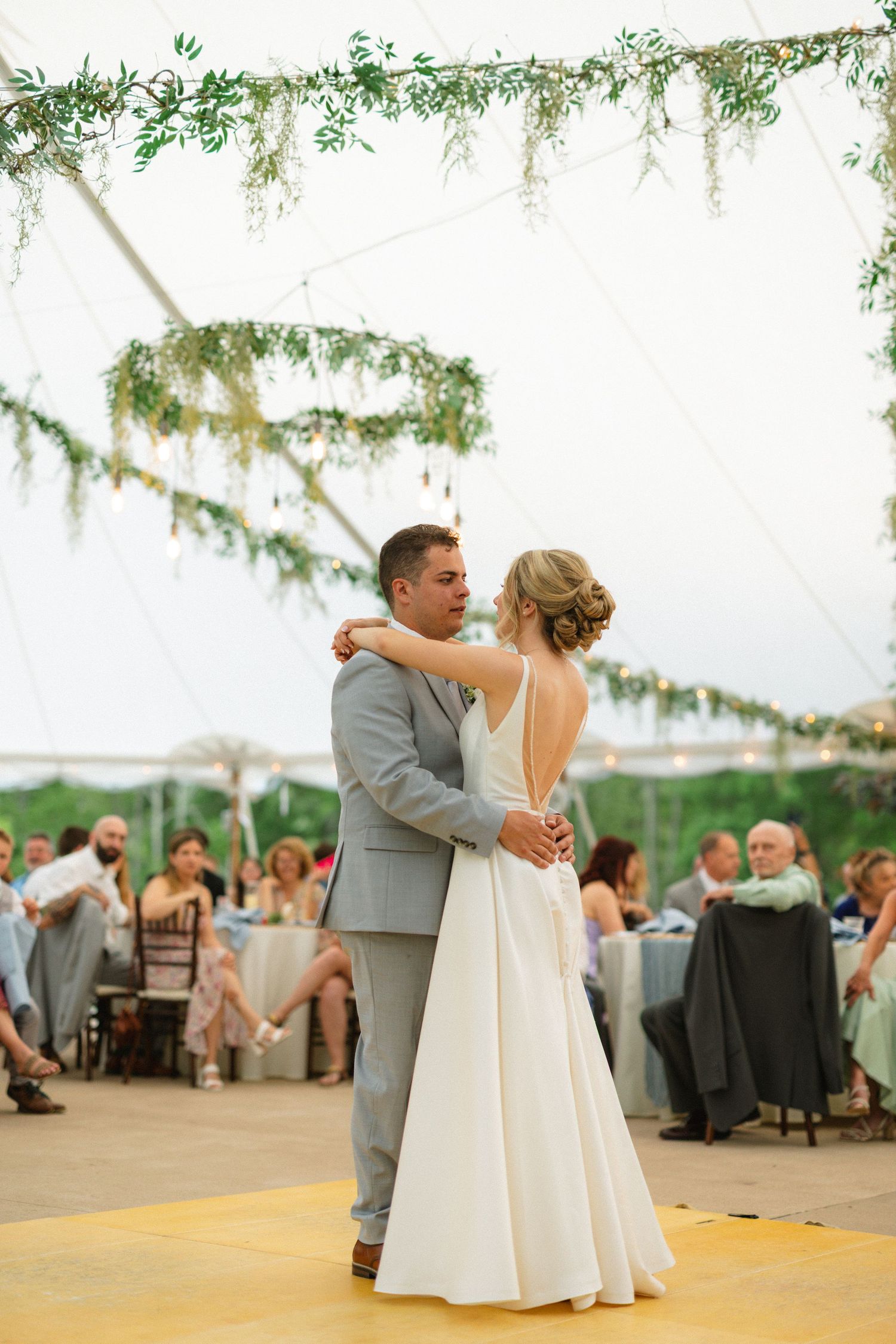 Bride and groom share their first dance under a floral-adorned tent at an outdoor wedding reception.
