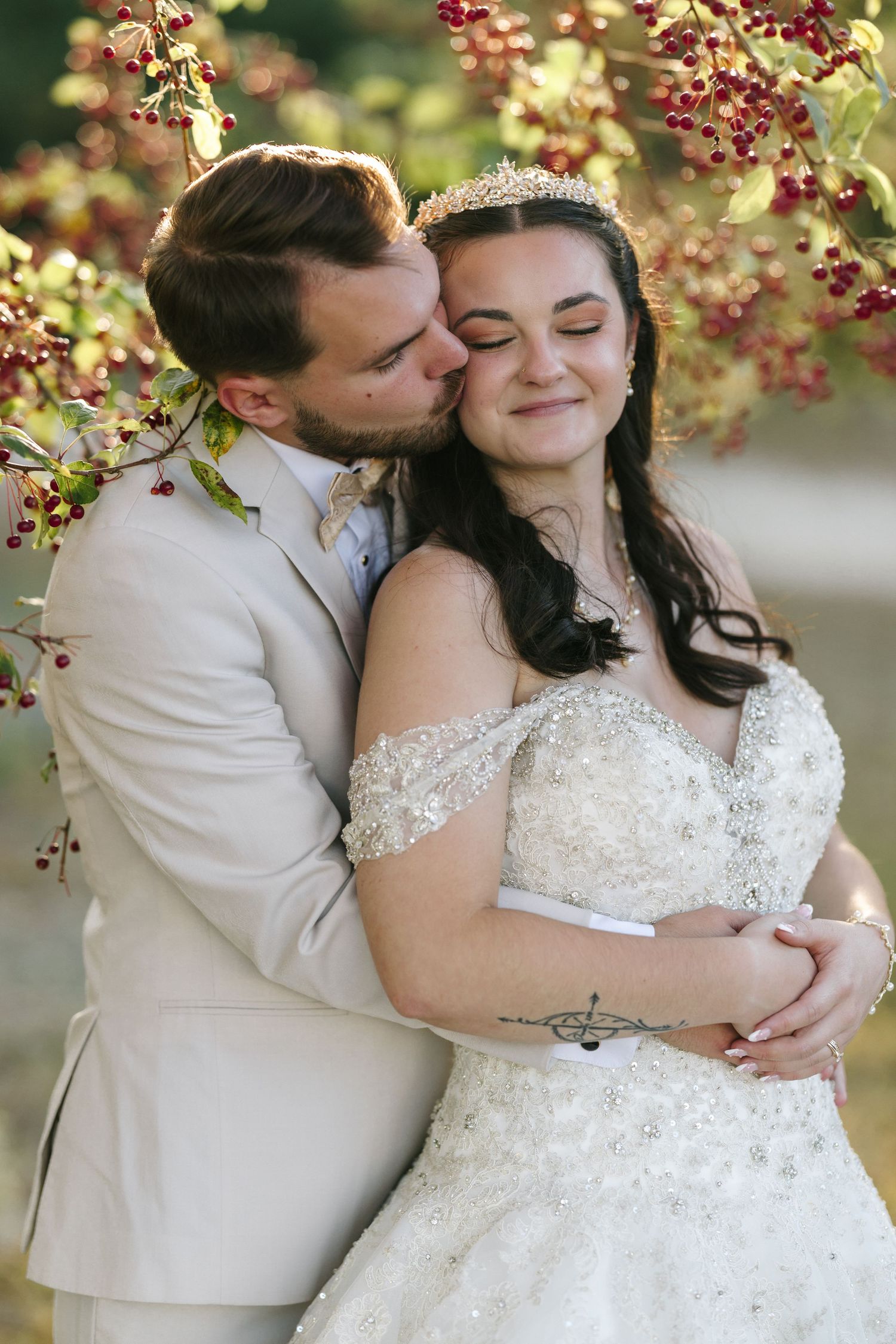 Romantic wedding couple embracing under autumn berries in outdoor setting.