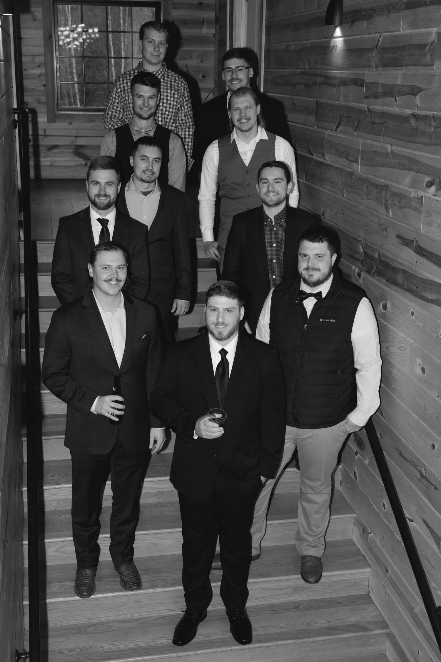 A group of formally dressed men in black suits and vests walking down wooden stairs in a modern interior setting.