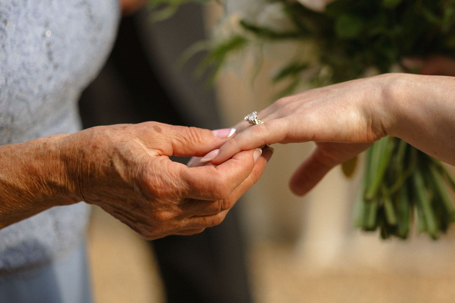 Close-up of hands exchanging a diamond engagement ring during a wedding ceremony.