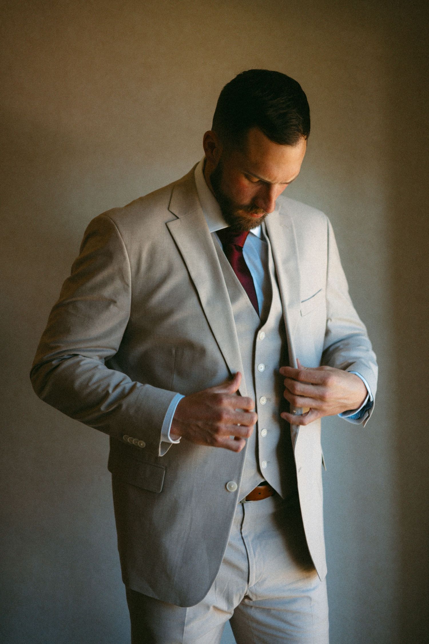 A groom adjusts his light gray suit jacket while getting ready for the ceremony.