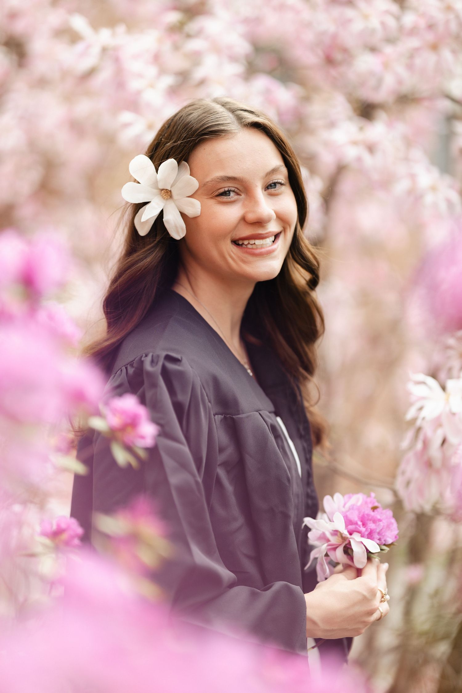 Graduate portrait session among blooming pink cherry blossoms with soft natural lighting.