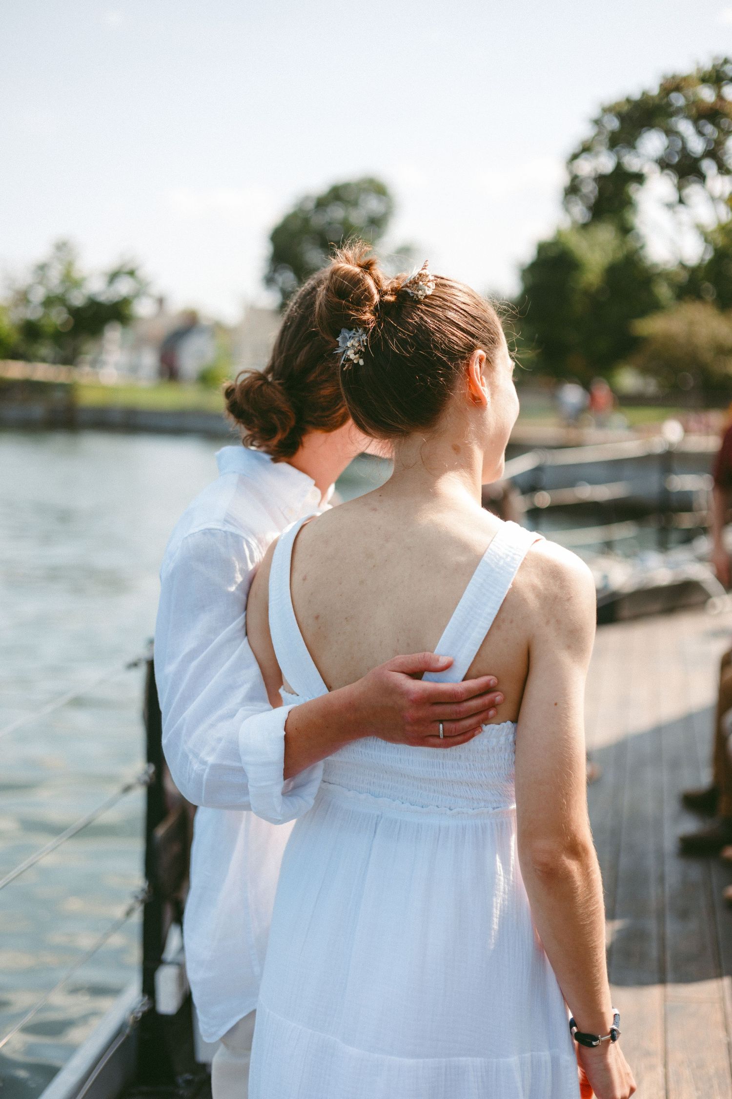 Couple in white summer clothing standing by a waterfront dock.