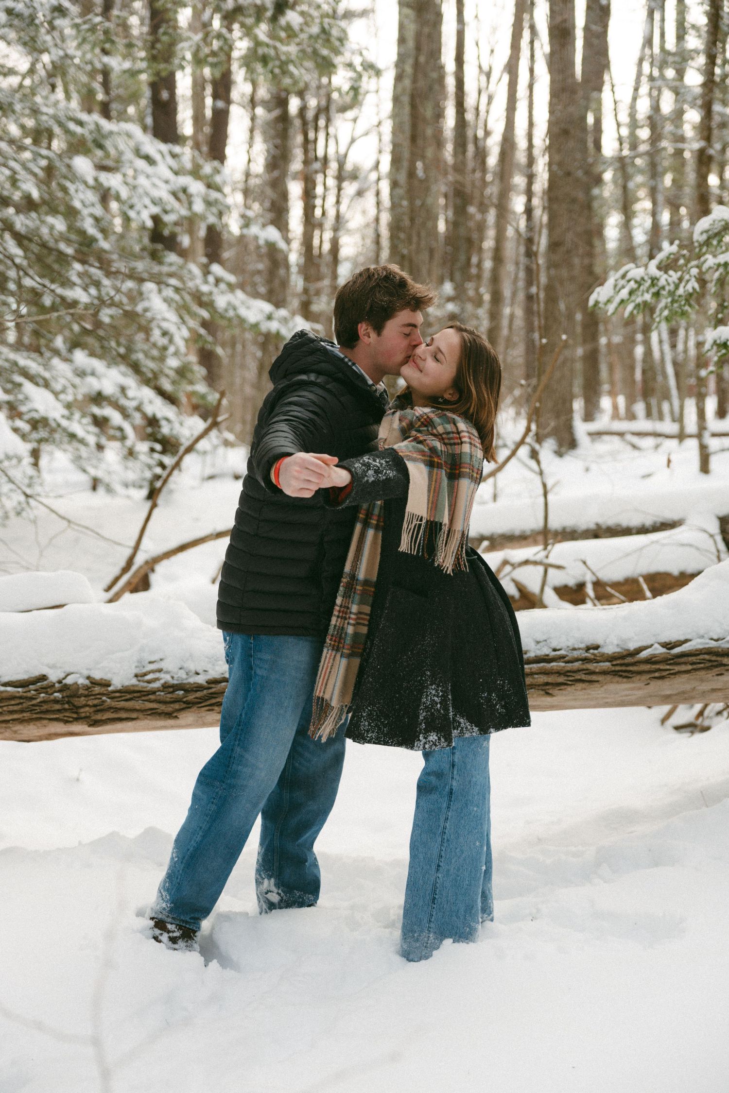 A romantic winter engagement photo sequence shows a couple in matching black coats sharing a kiss in the snowy woods.