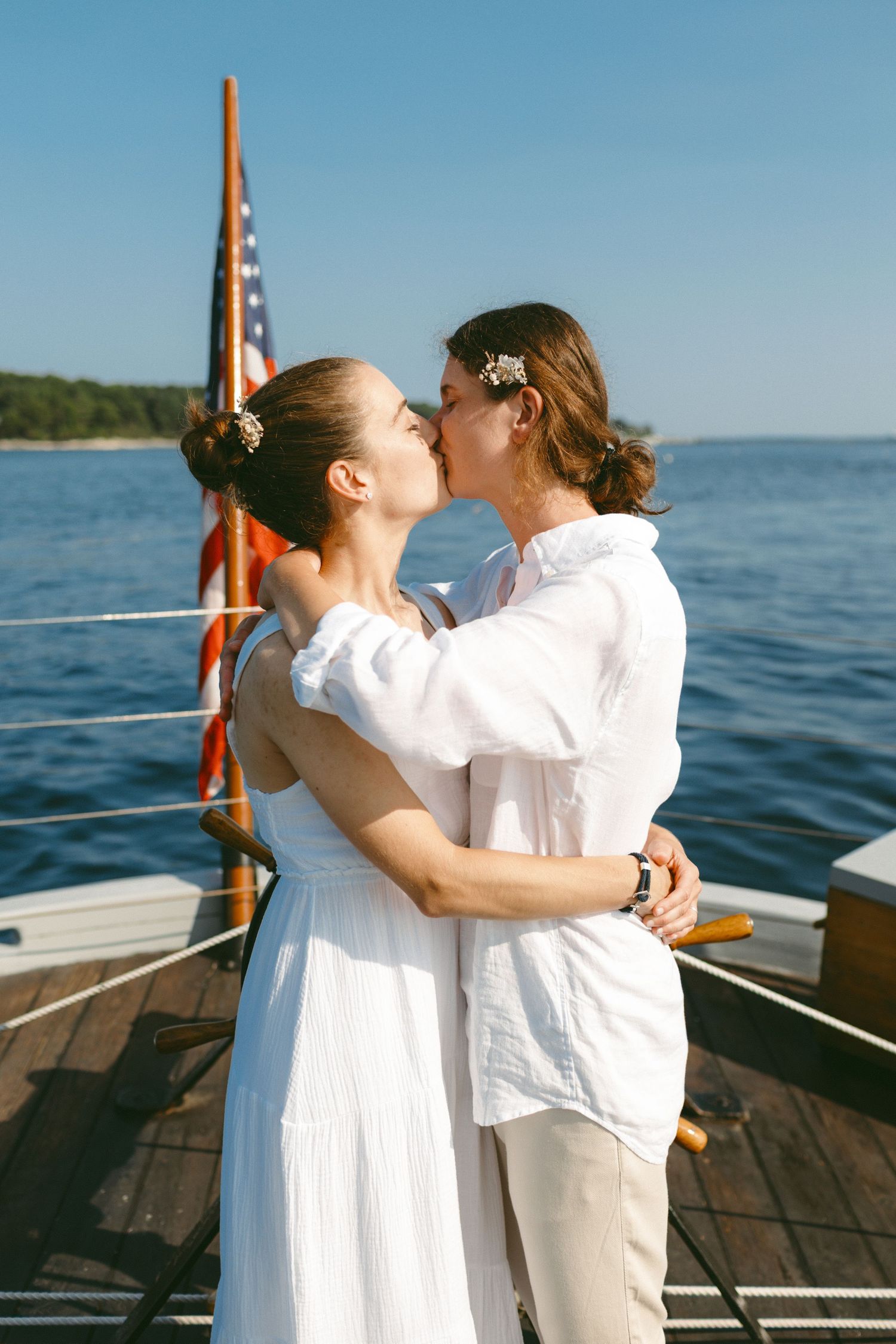 Couple embracing on boat deck with American flag and coastline visible in background.