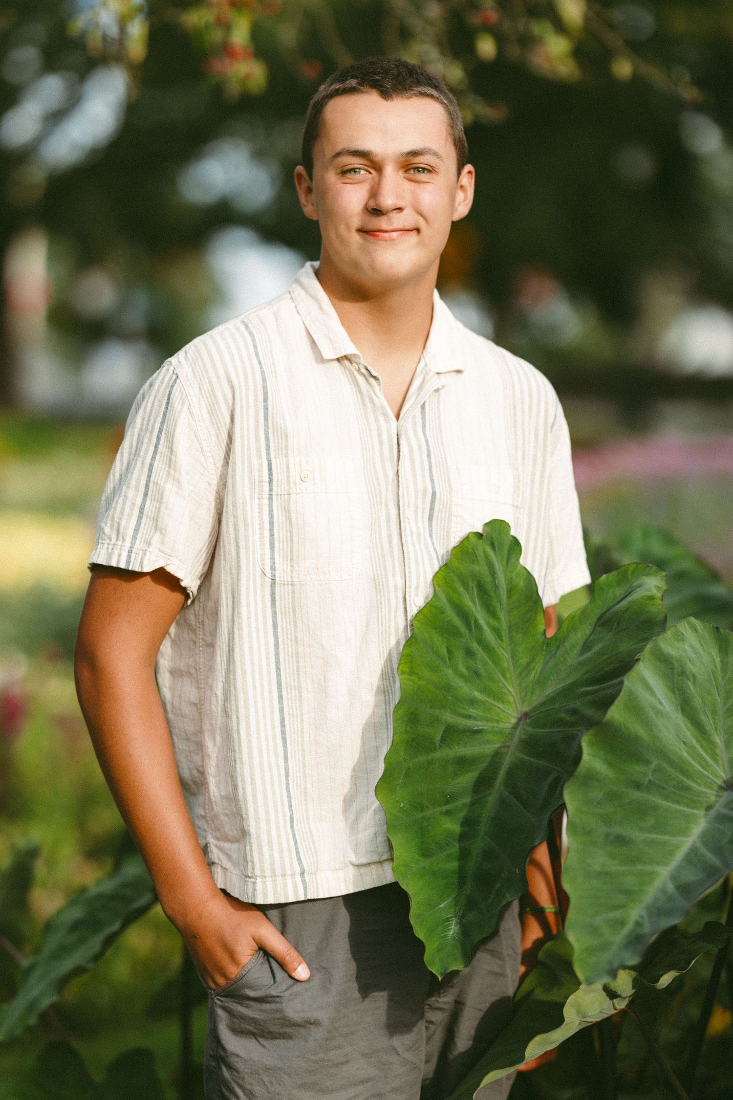 Portrait in white shirt beside large tropical leaves in garden setting.