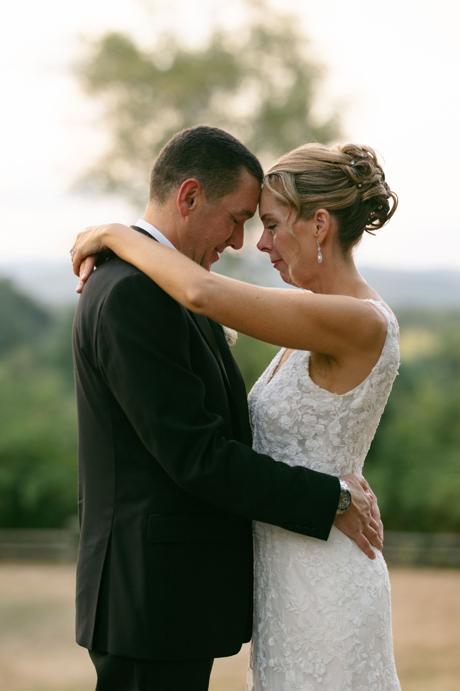A couple shares a romantic dance together outdoors, with the bride wearing a white lace dress and groom in black attire.