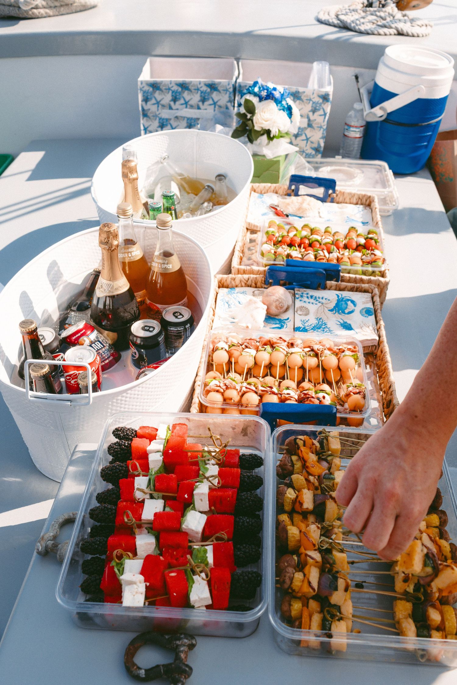 Catering spread on a boat deck with appetizers, drinks and snacks laid out in containers.
