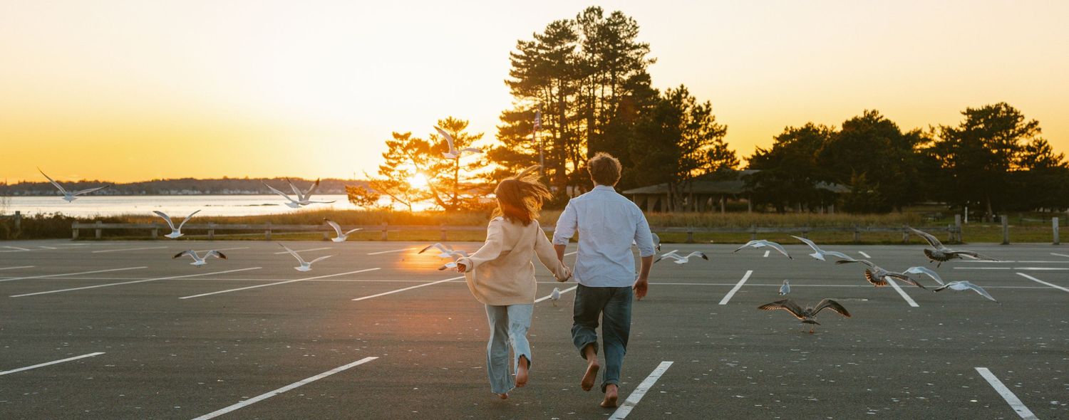 A group of people play basketball on an outdoor court at sunset with golden light illuminating the scene.