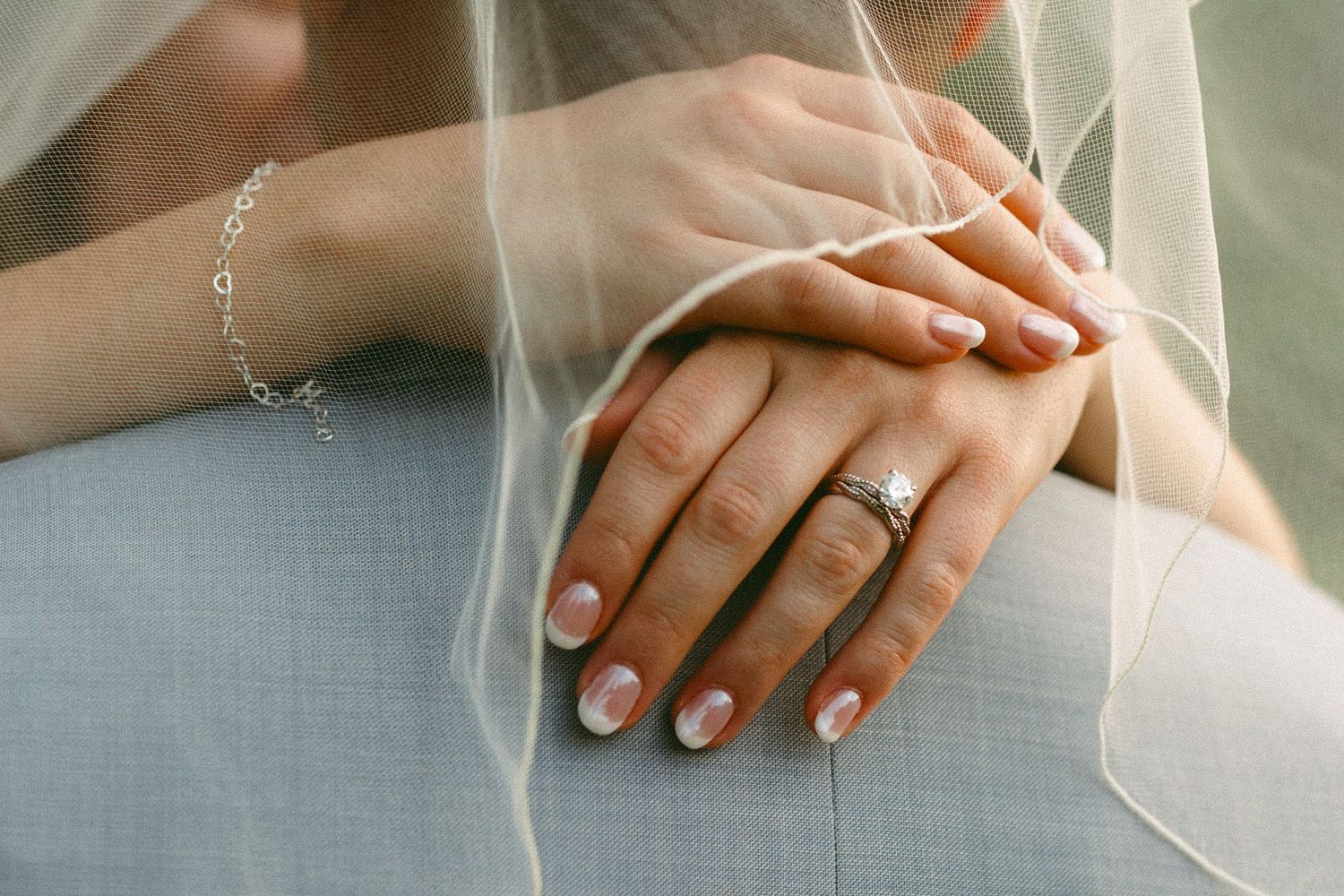 Close-up of bride's hands showing diamond engagement ring and delicate bracelet beneath a sheer wedding veil.