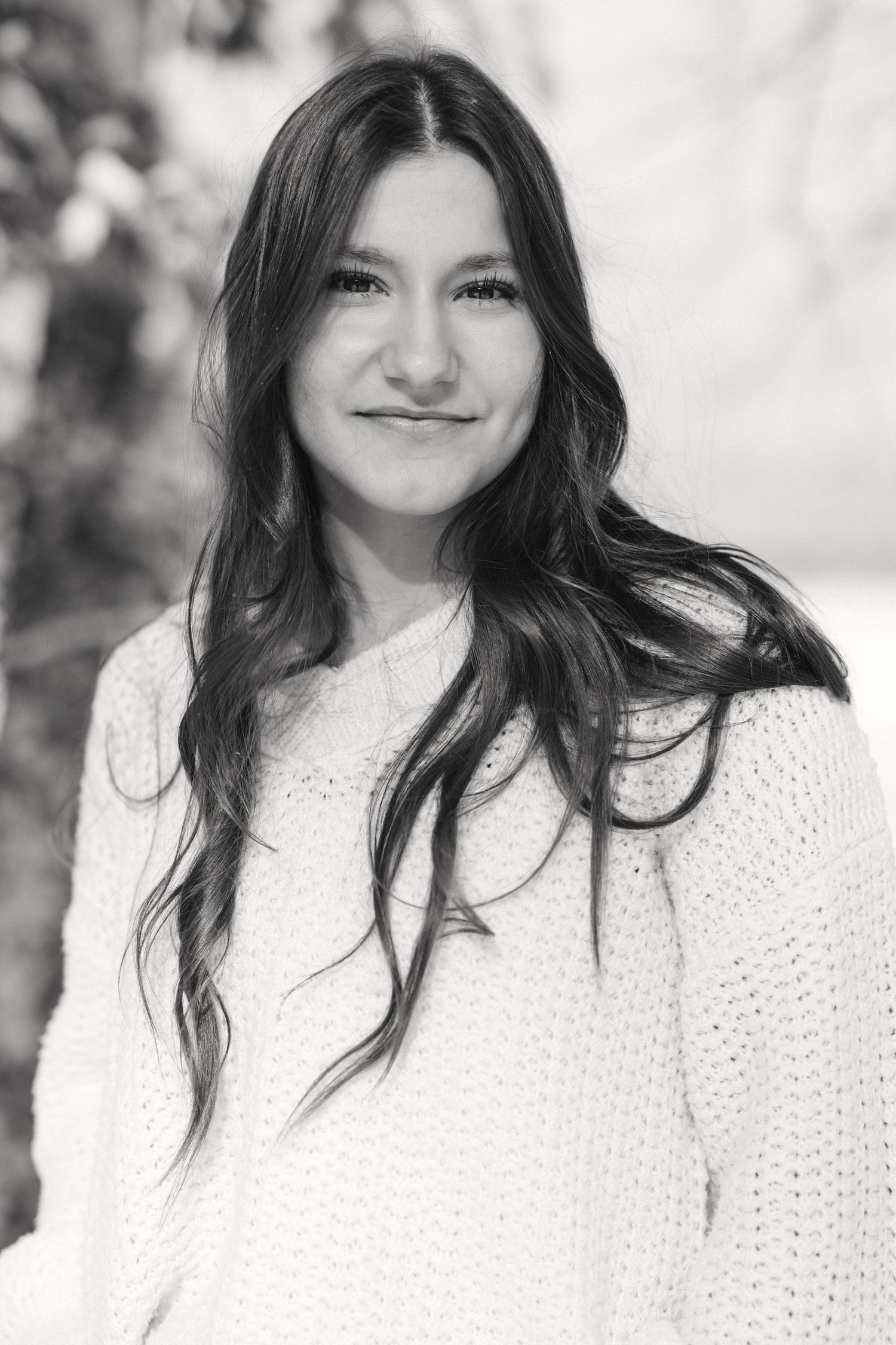 A person with long dark hair wearing a white knit sweater poses in a black and white portrait series.
