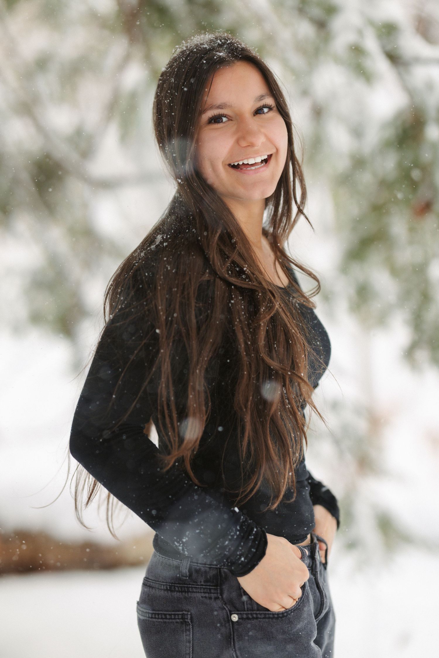 A person in a black jacket laughs joyfully while playing in the snow during winter.