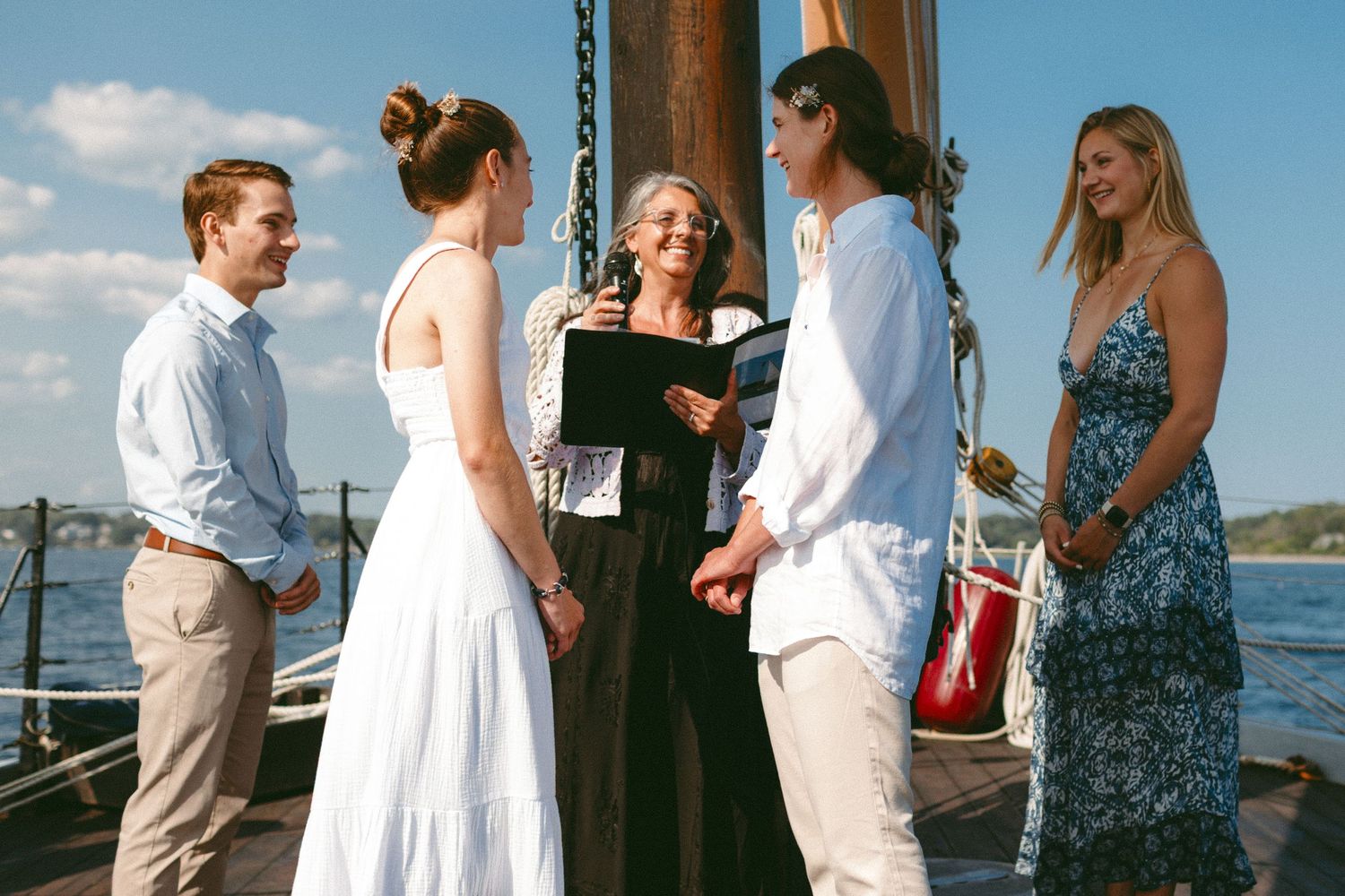 Intimate wedding ceremony being conducted on a sailboat deck with guests watching.