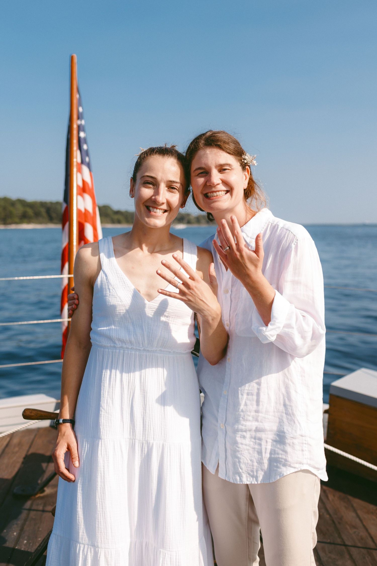 Two people in white showing off rings on boat deck with American flag.