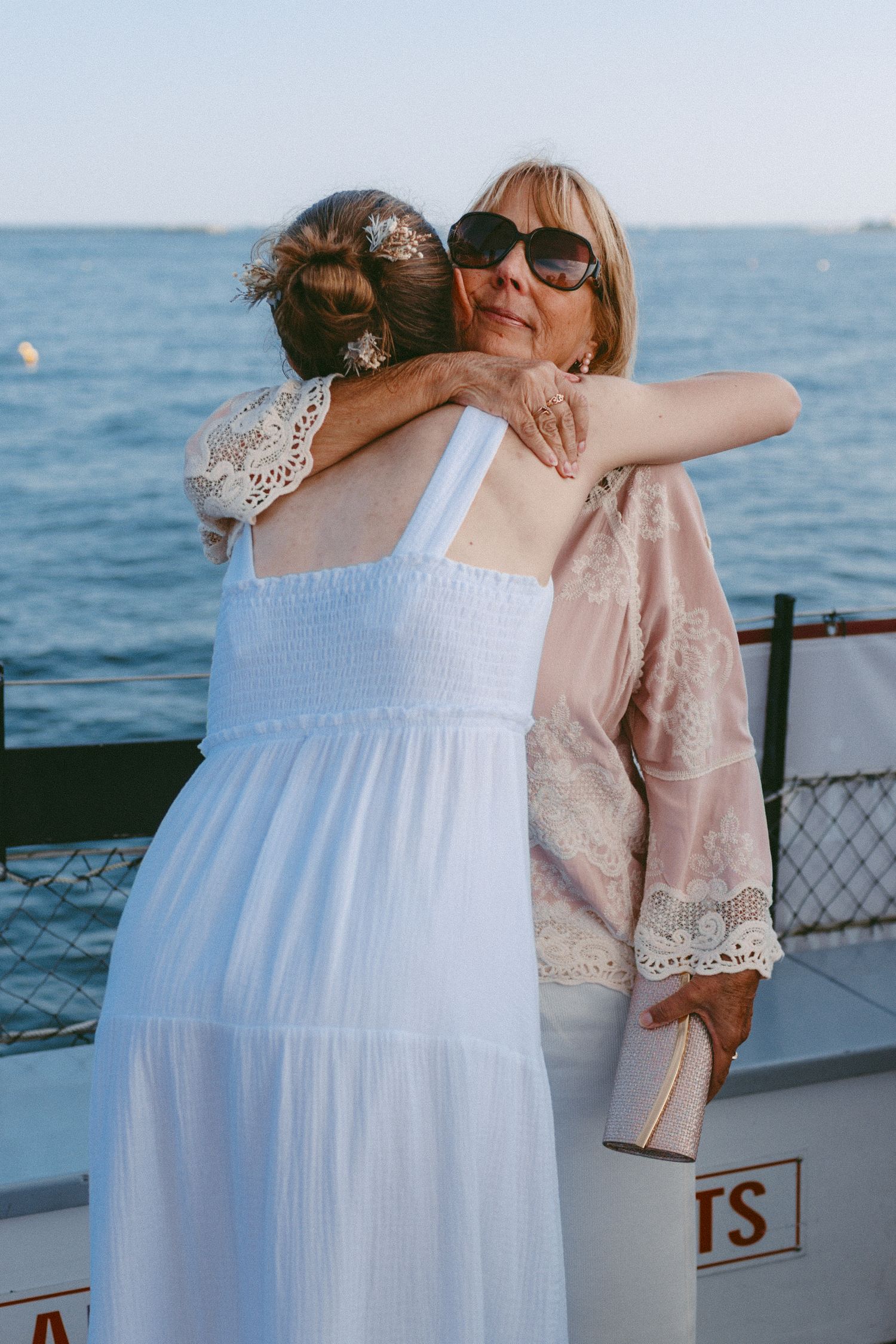 Two people embrace on a boat deck with blue ocean waters in the background.