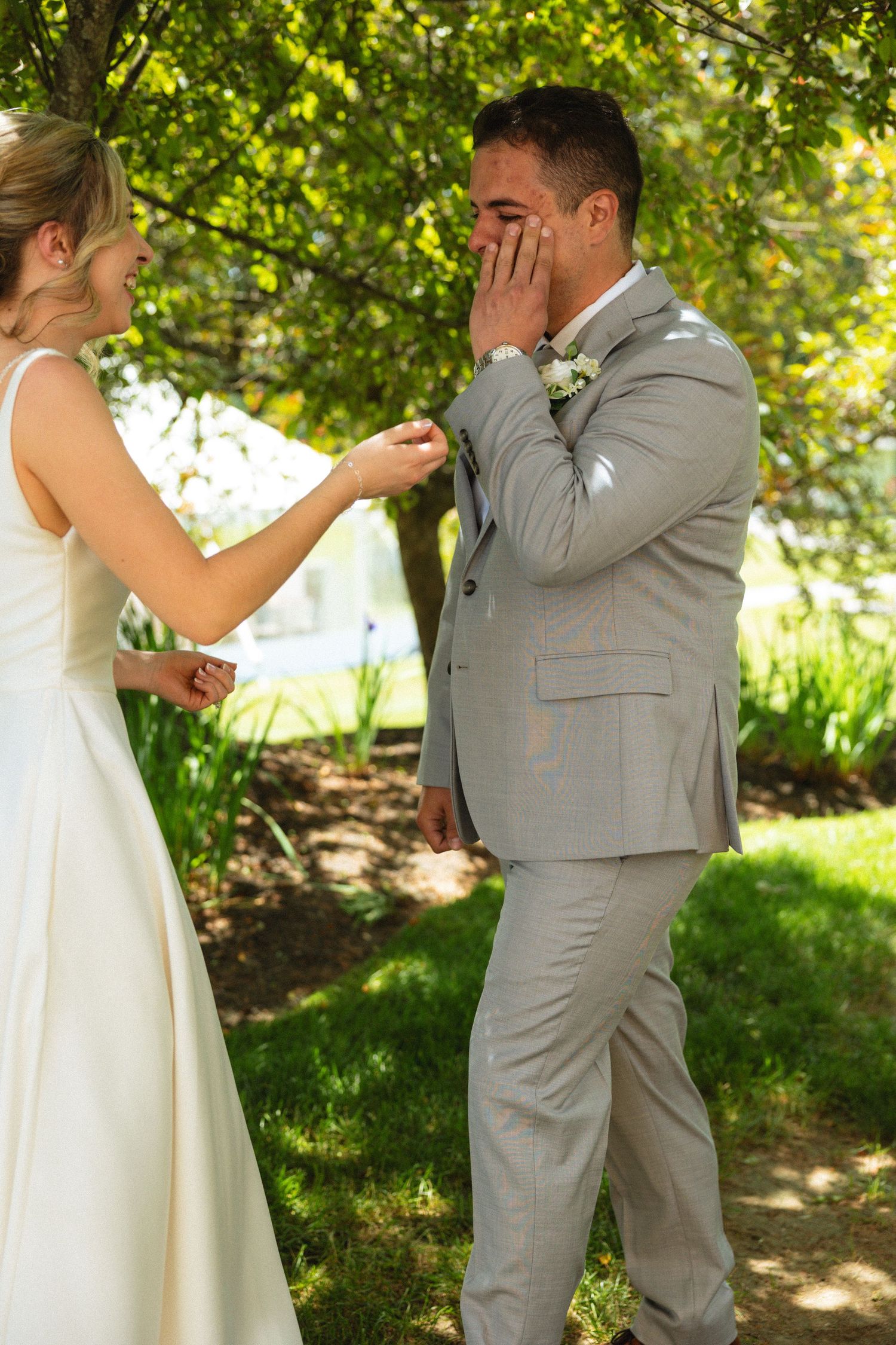 Emotional groom covering his mouth in tears during first look with bride in white dress outdoors.