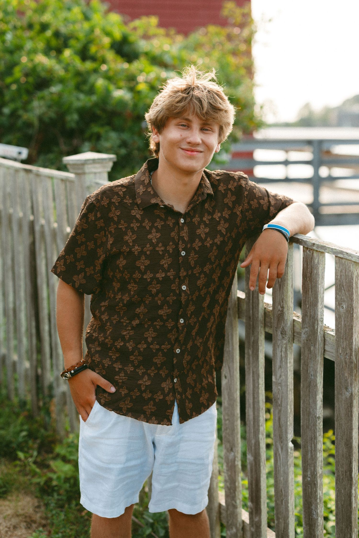 Casual portrait series against wooden fence with brown patterned shirt and light shorts.