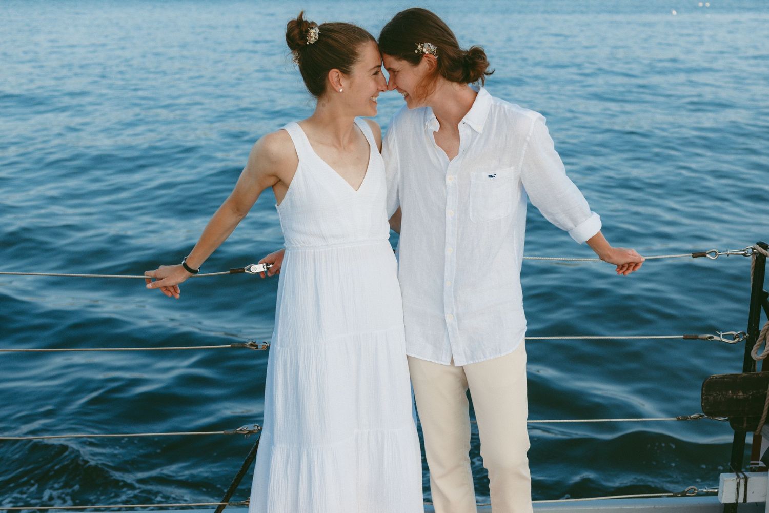 A couple in white outfits shares a romantic moment by the ocean at sunset.