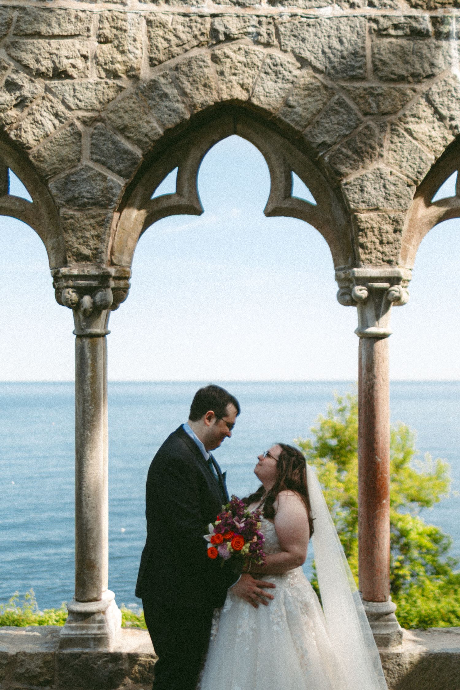 Wedding couple sharing intimate moments under stone arches overlooking the ocean.