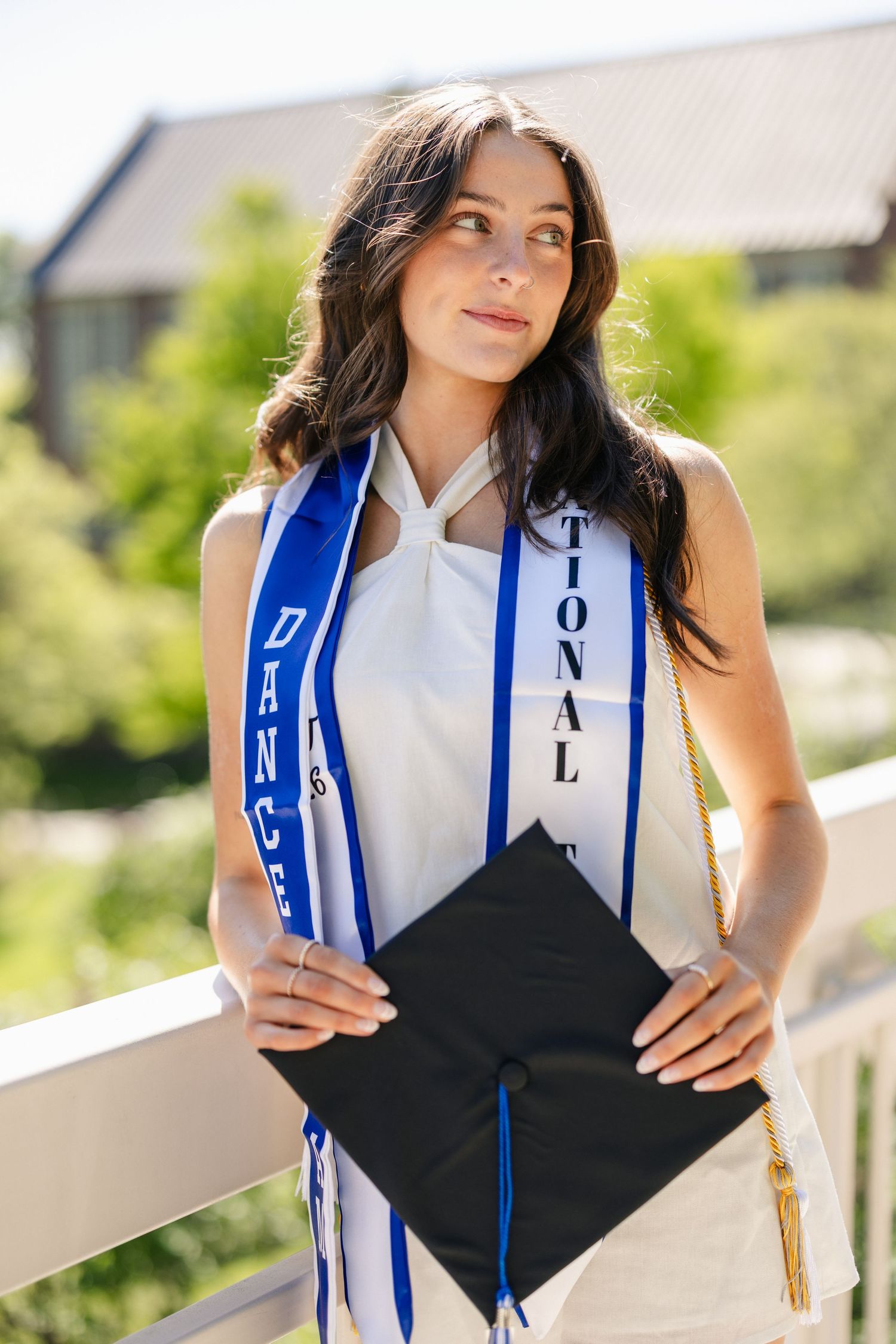 Graduate wearing graduation stole with blue and gold tassels poses for photos outdoors.