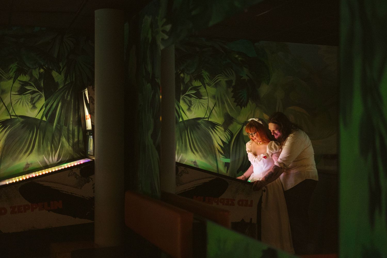 Two people in period costumes share an intimate moment on a dimly lit stage with lush tropical jungle backdrop.