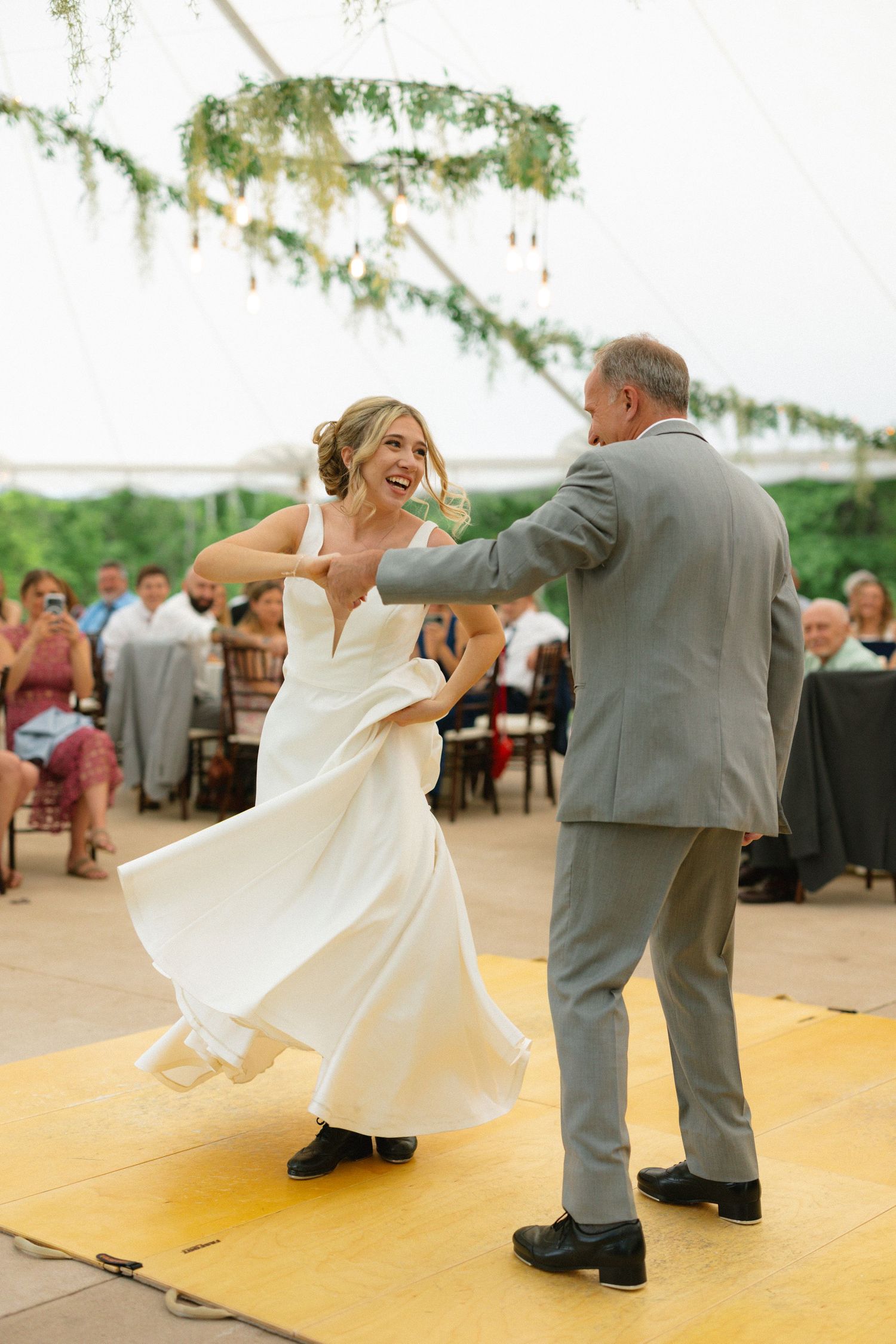 Joyful bride in white gown twirling during energetic father-daughter dance at tented reception.