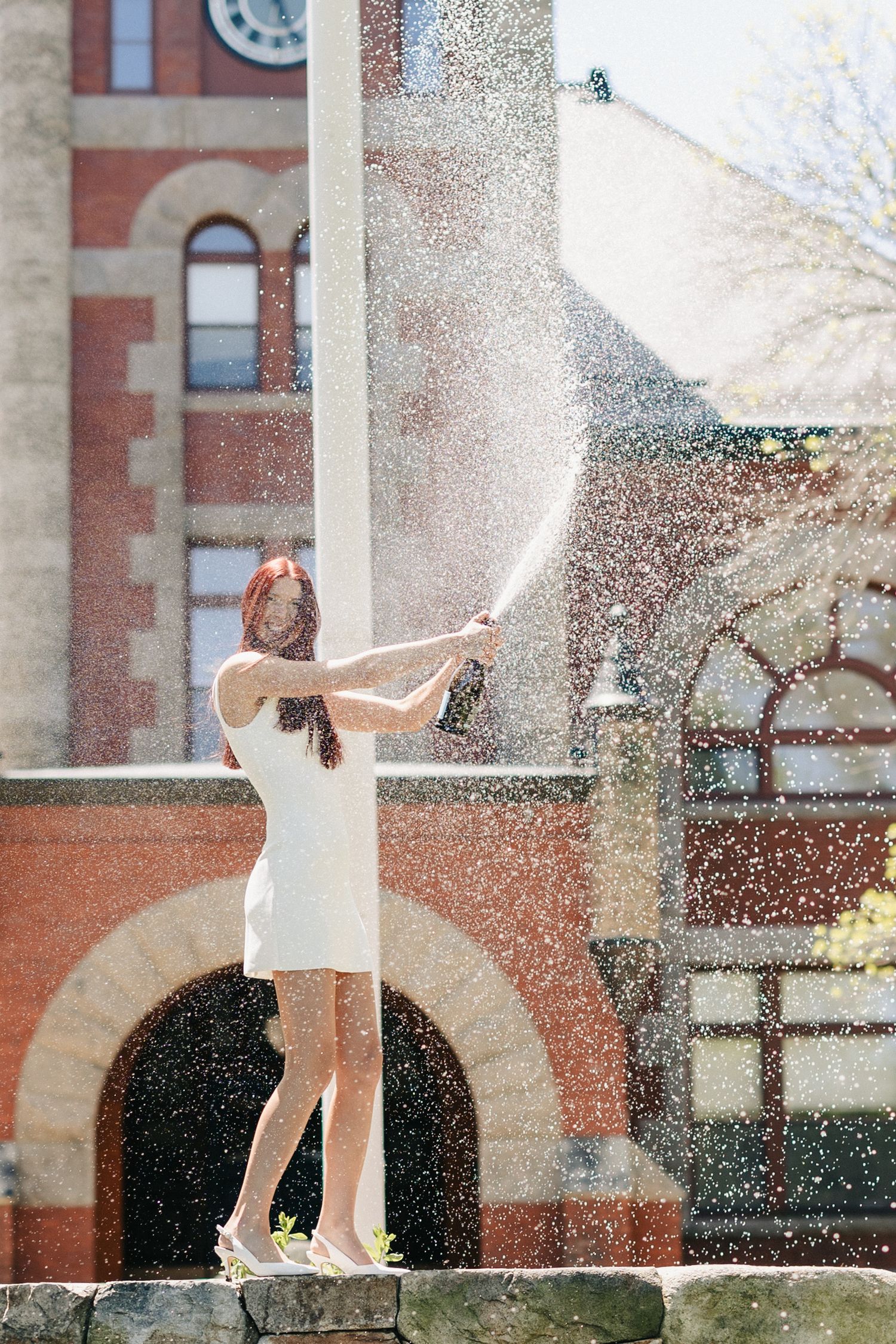 Graduate celebrating with water splashing in front of brick building.