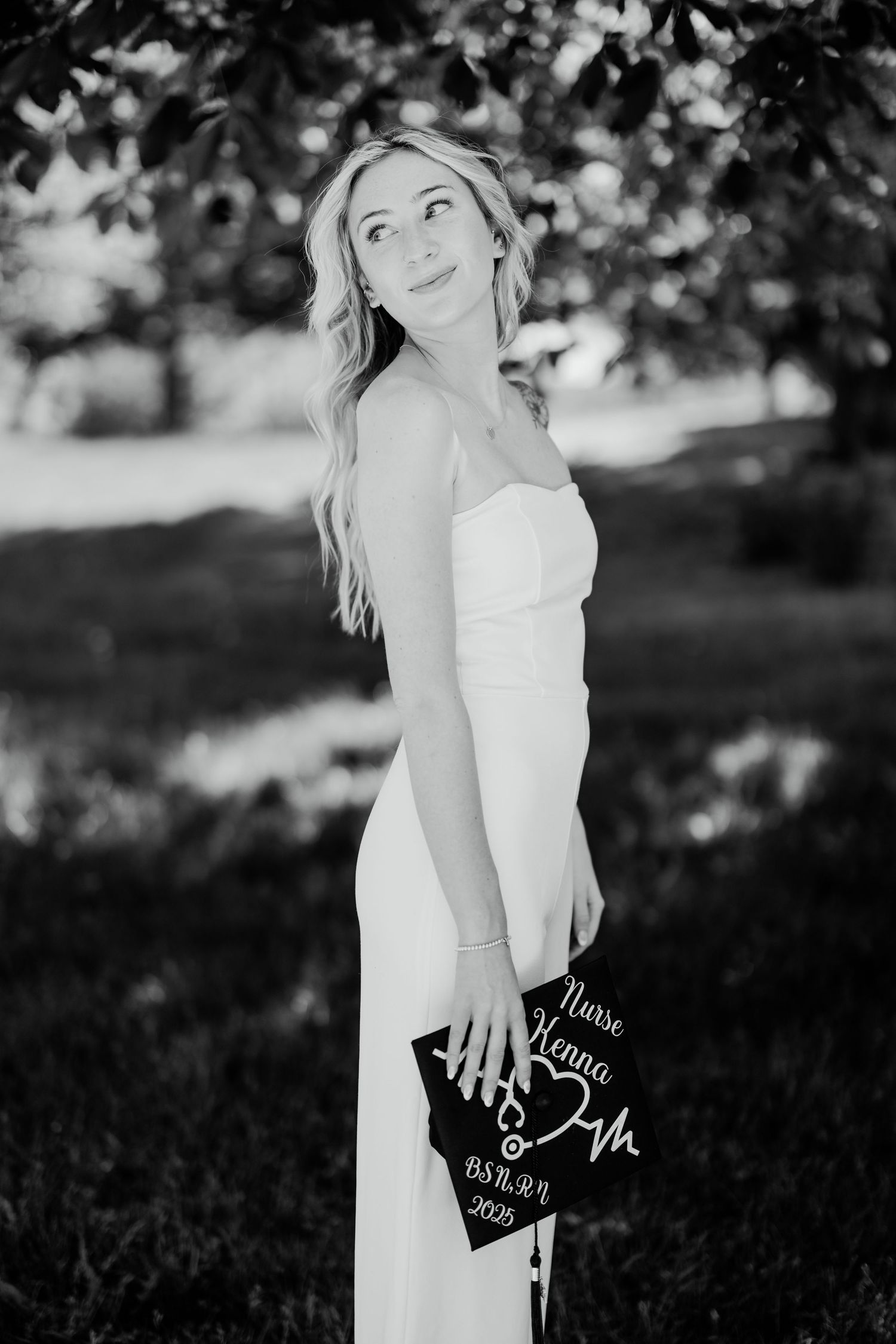 Black and white portrait of graduate holding decorated cap in outdoor setting.