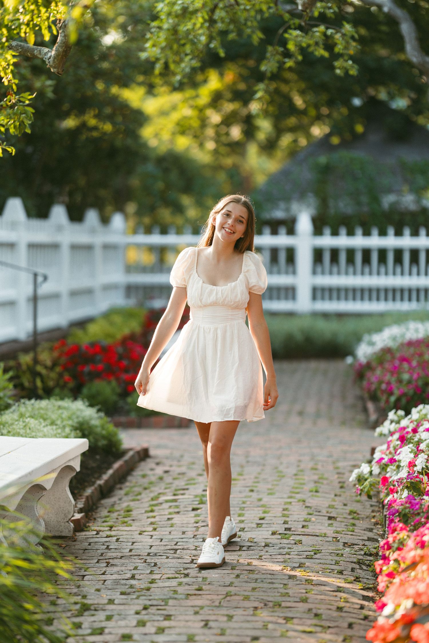 White dress twirling along a garden path with pink flowers and white fence.