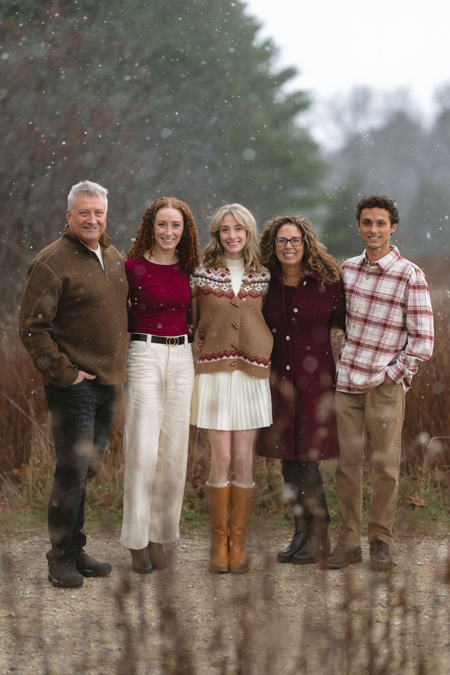 Family group wearing burgundy and brown sweaters poses in falling snow.