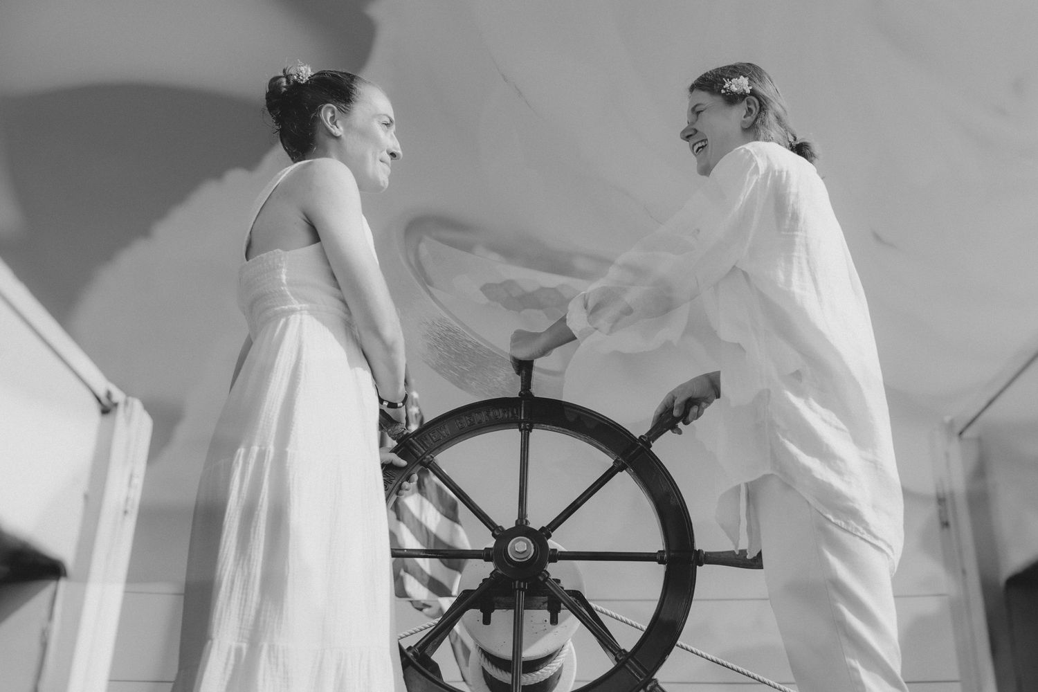 Black and white photo of two people at a ship's wheel during a nautical ceremony.