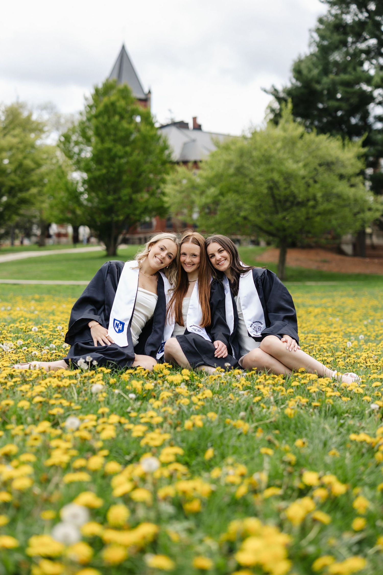 Graduates lying in field of yellow dandelions wearing academic regalia.