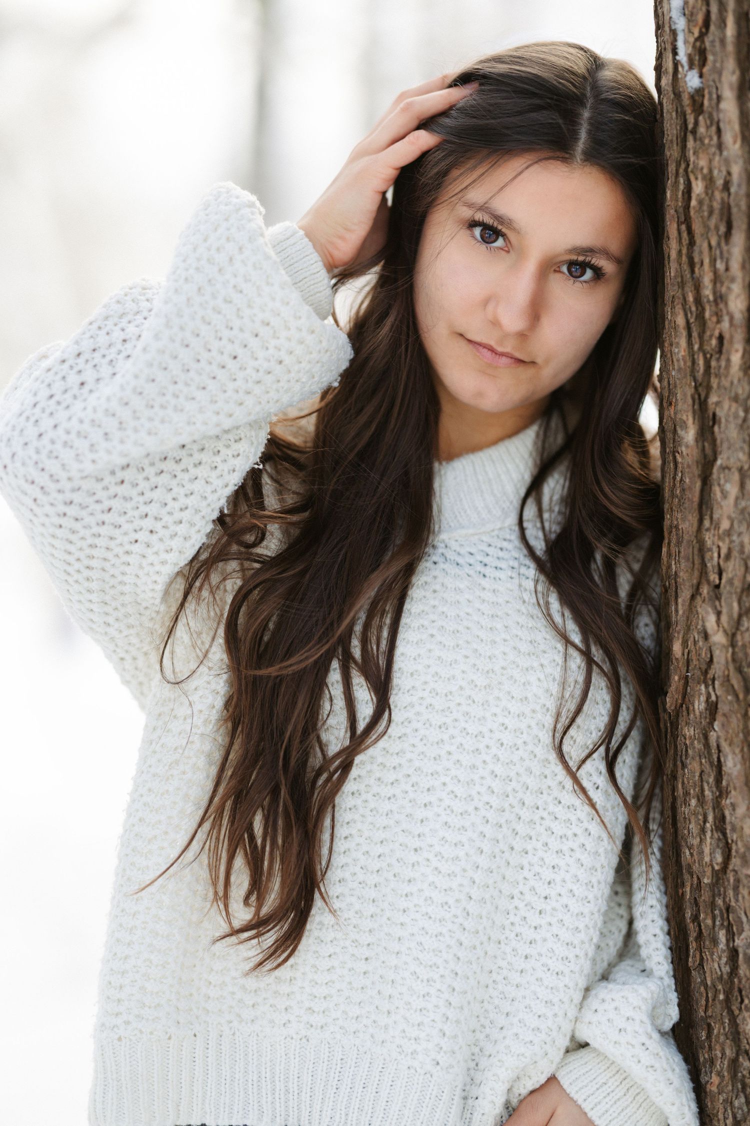 A person in a cozy white knit sweater poses against a tree trunk in a casual outdoor portrait series.