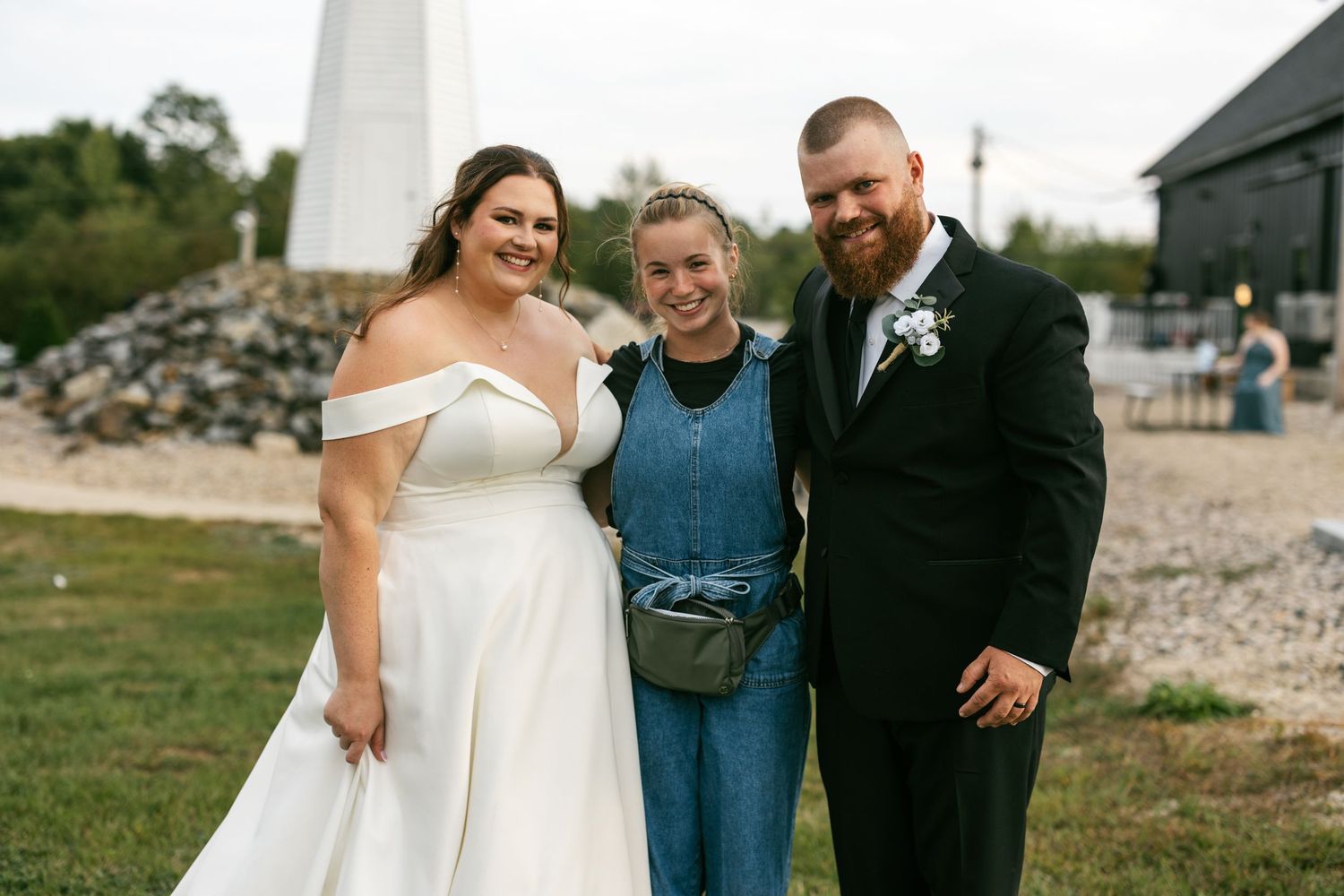 A wedding celebration takes place outdoors near a lighthouse on a sunny day.
