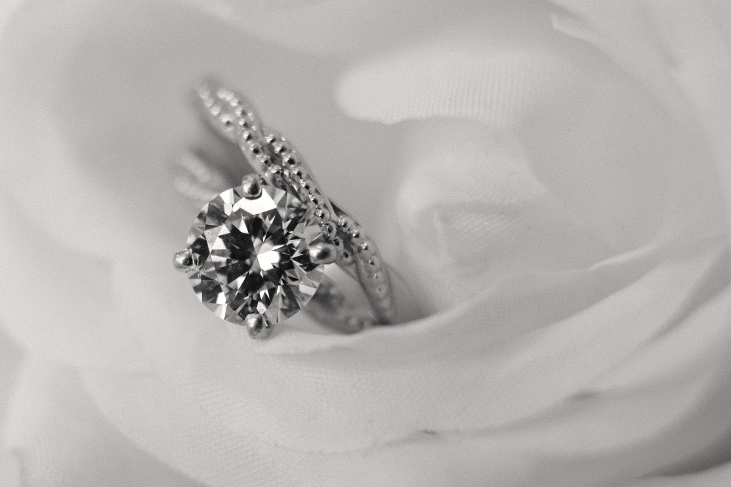 A sparkling round diamond solitaire engagement ring resting elegantly inside a white rose bloom.