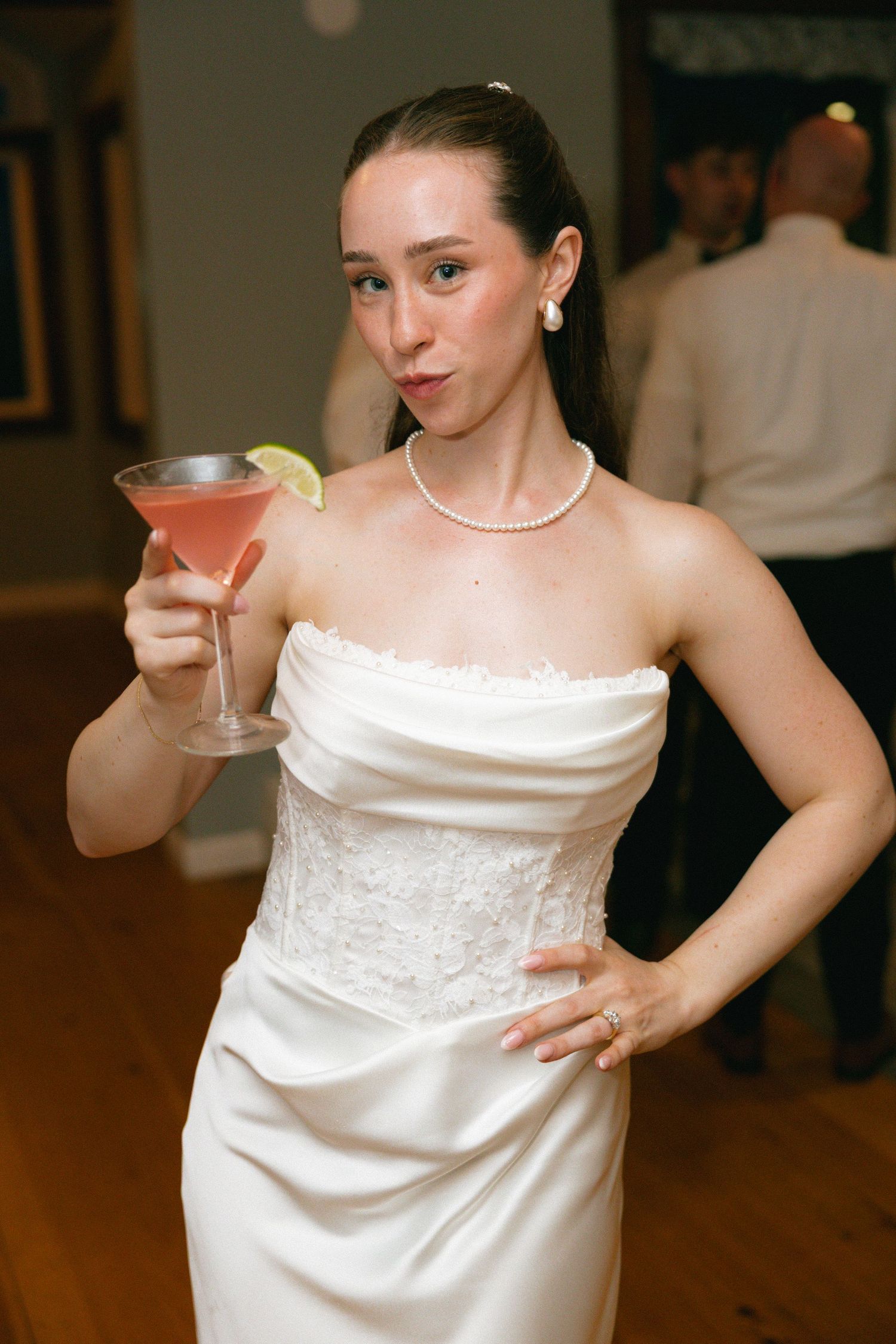 Bride in strapless white wedding gown holding a pink cocktail martini glass at reception.