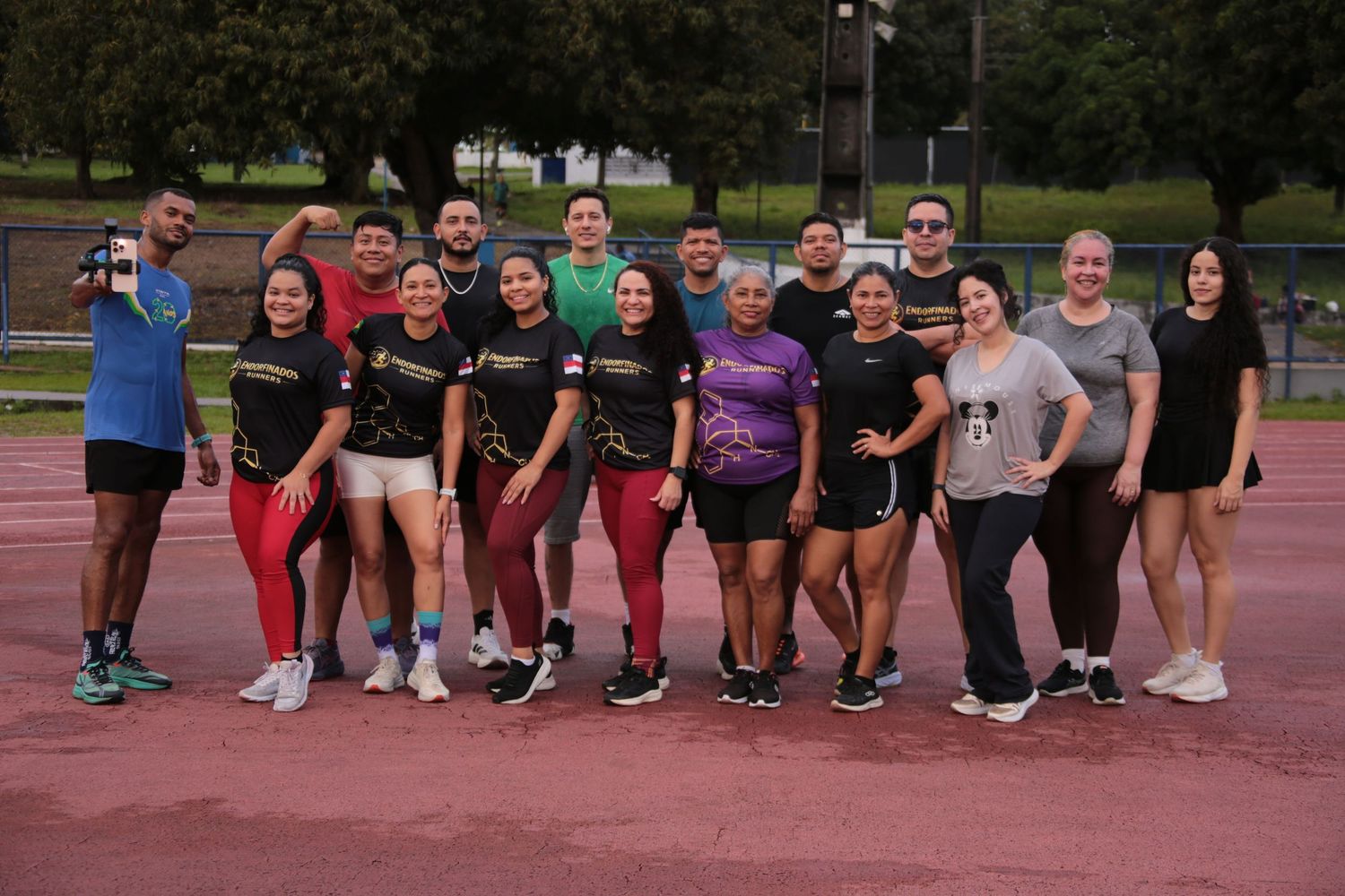 Group of athletes posing together on a red running track during outdoor fitness training session.